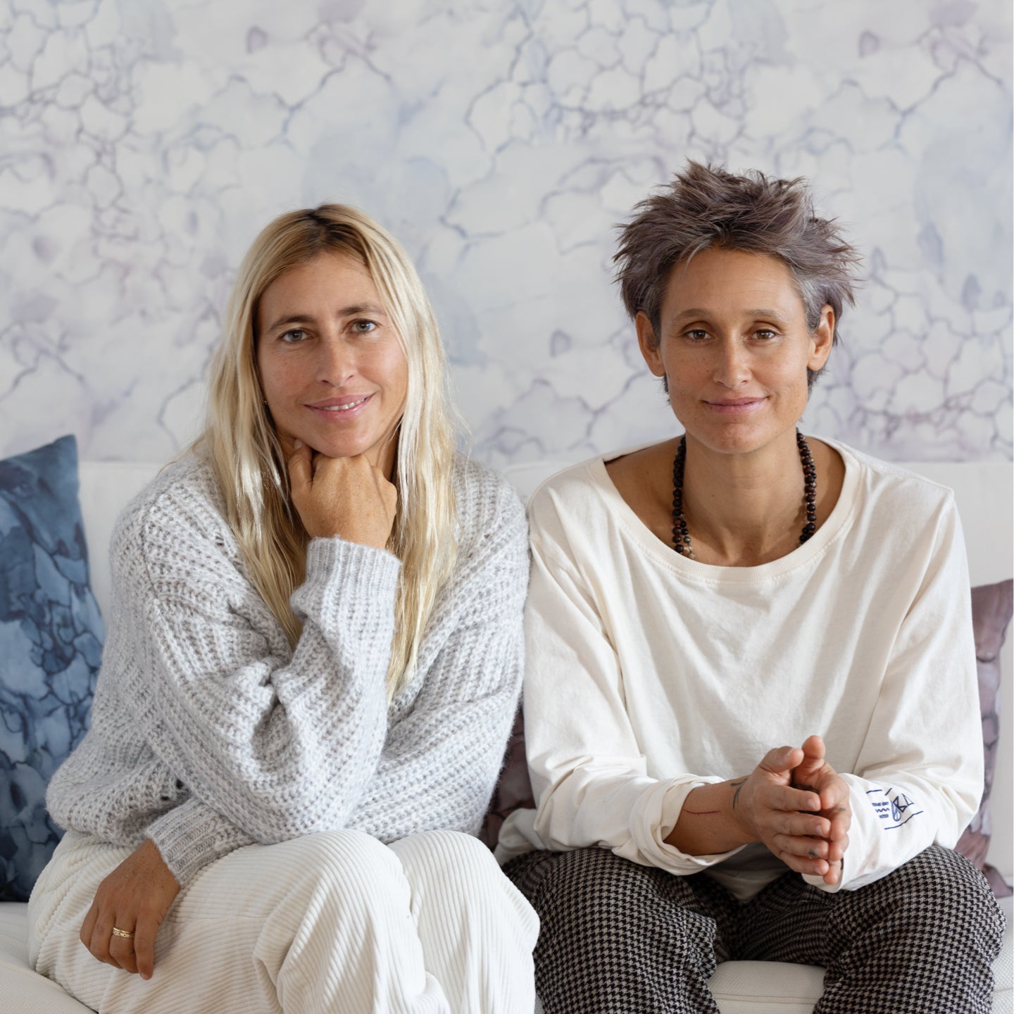 Two women sitting on a couch in front of a wall
