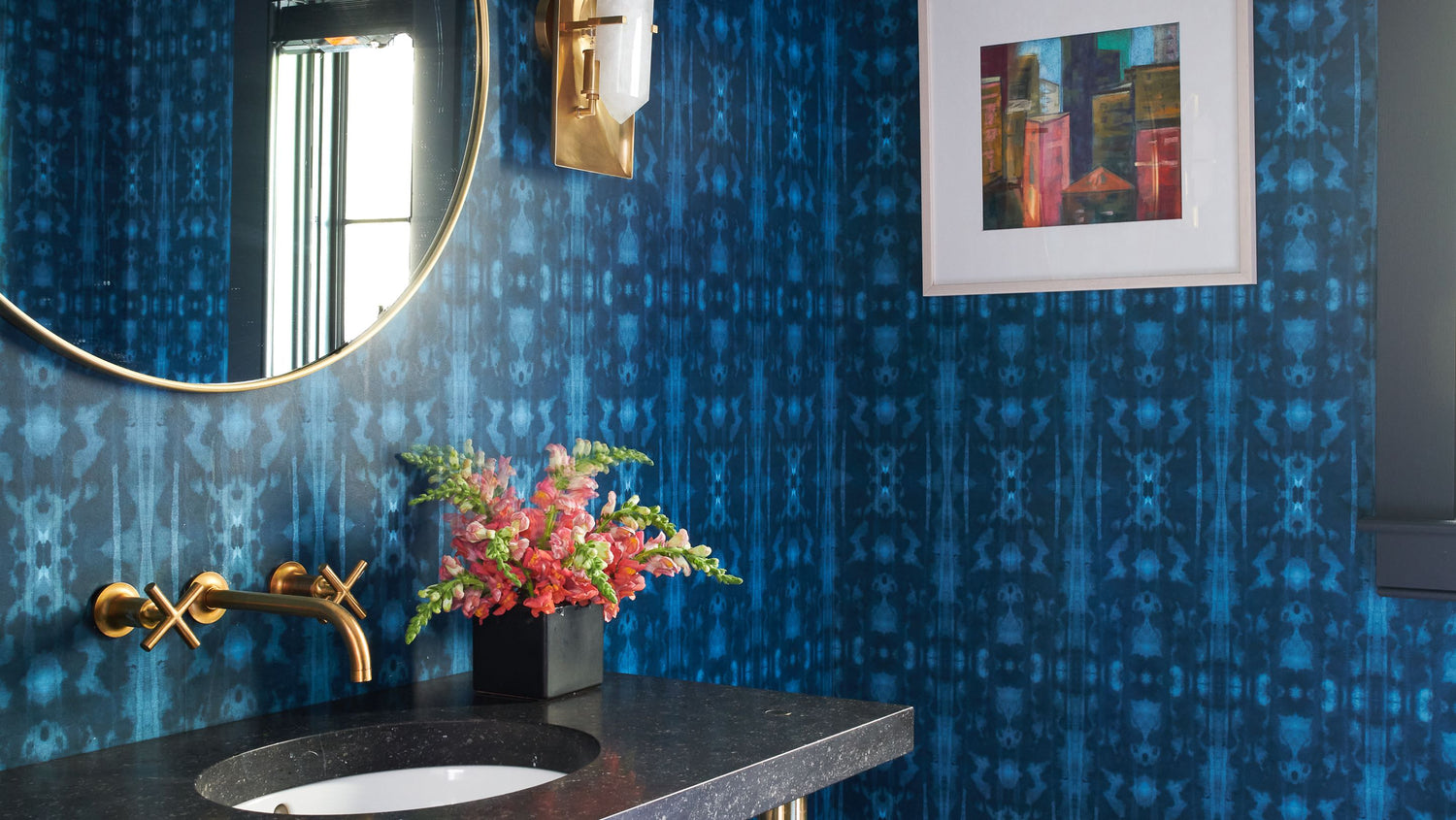 A bathroom with blue wallpaper and a gold mirror