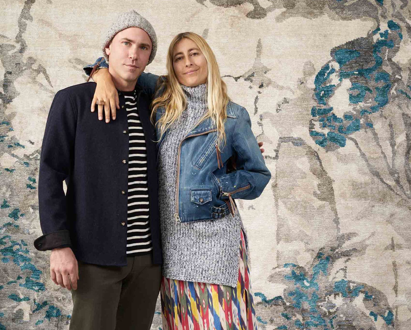 A man and woman posing for a photo in front of a floral wallpaper