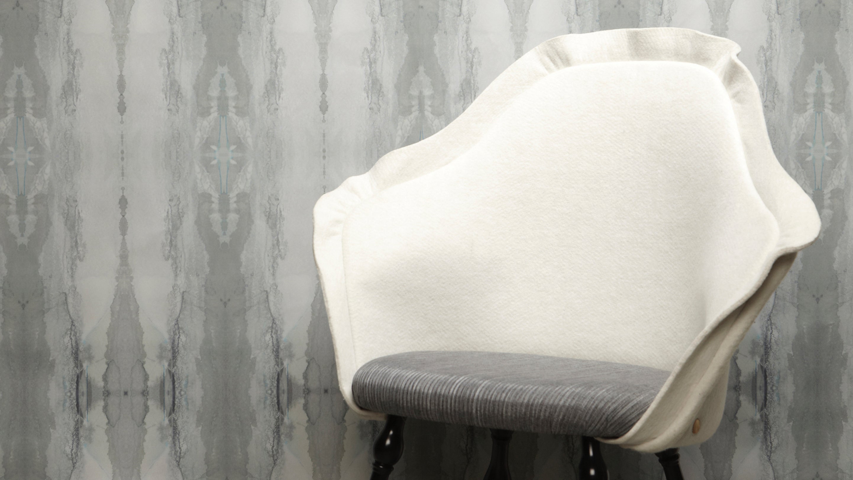 A white chair in front of a gray wallpaper