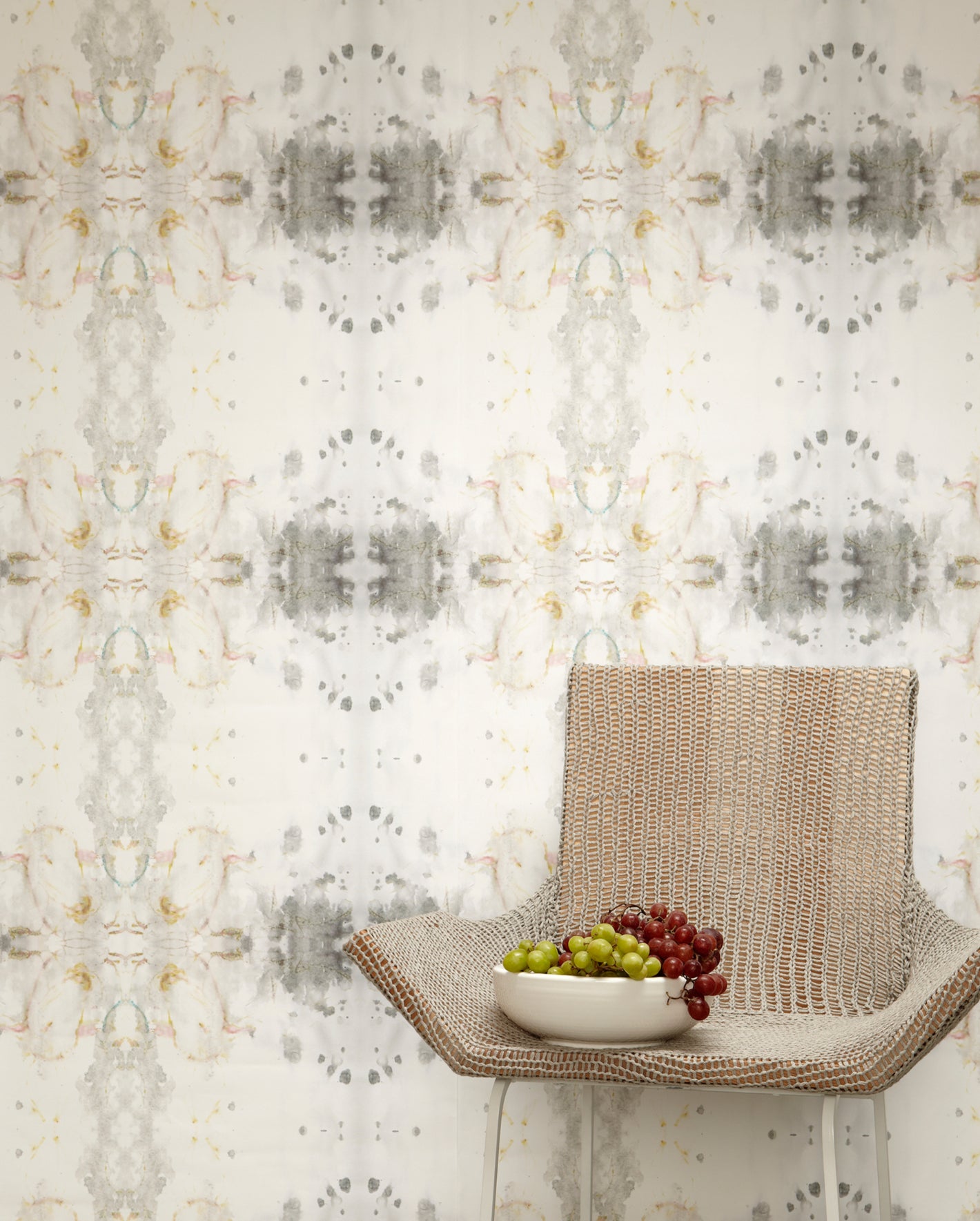 A chair with a bowl of grapes in front of a wallpaper