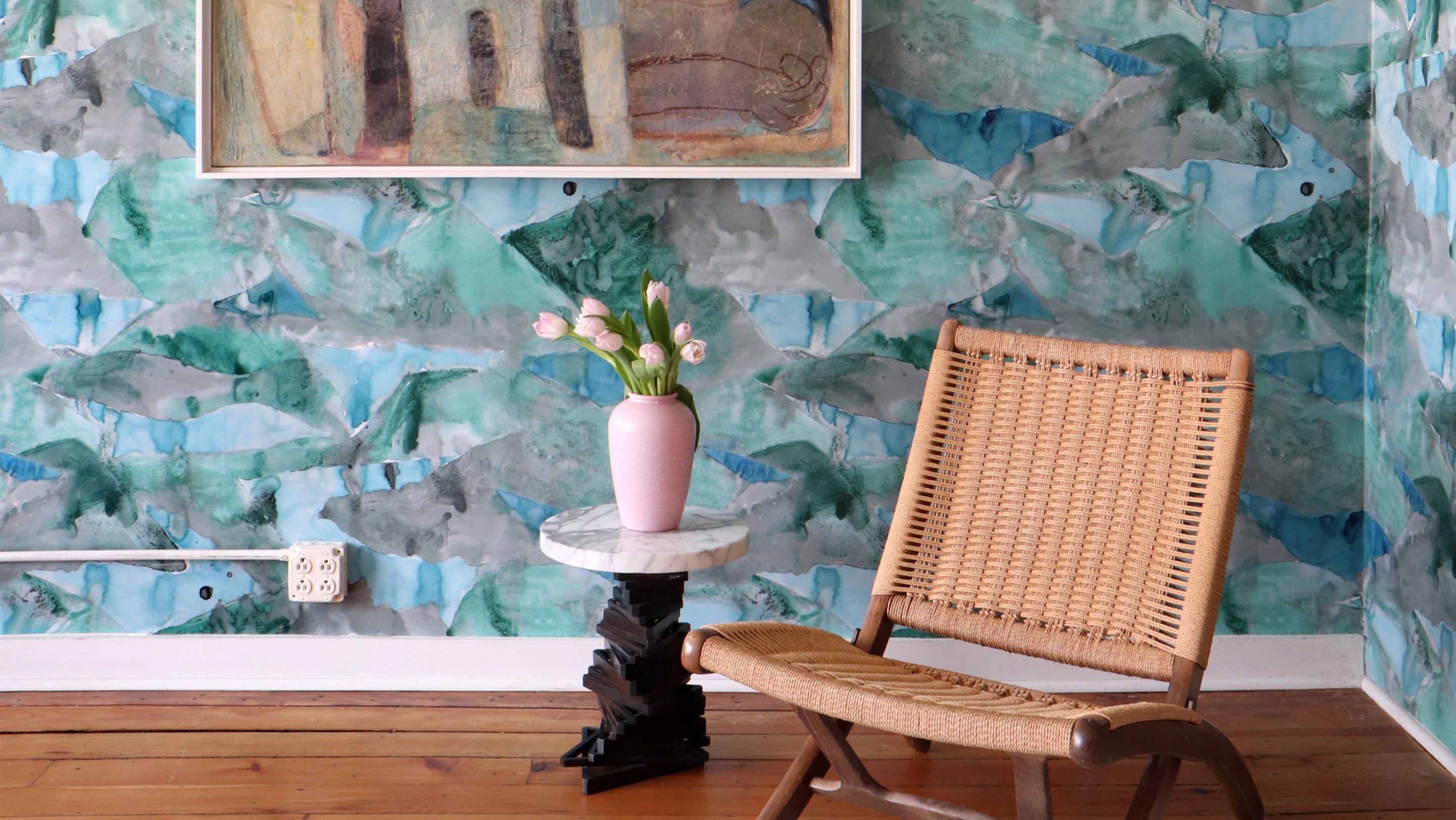 A wicker chair sits in front of a blue and green wallpaper