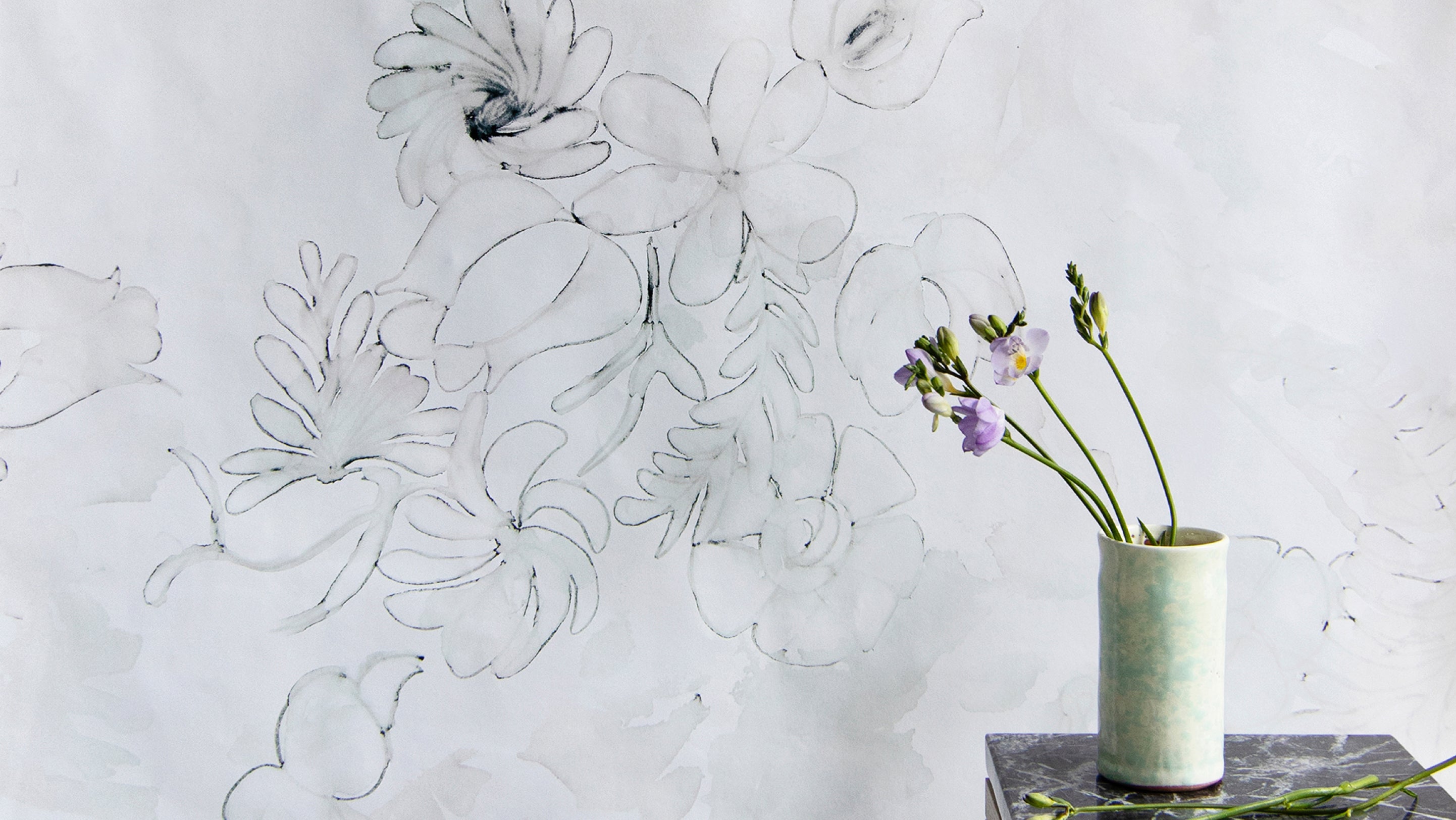 A vase with flowers on it in front of a wall with wallpaper