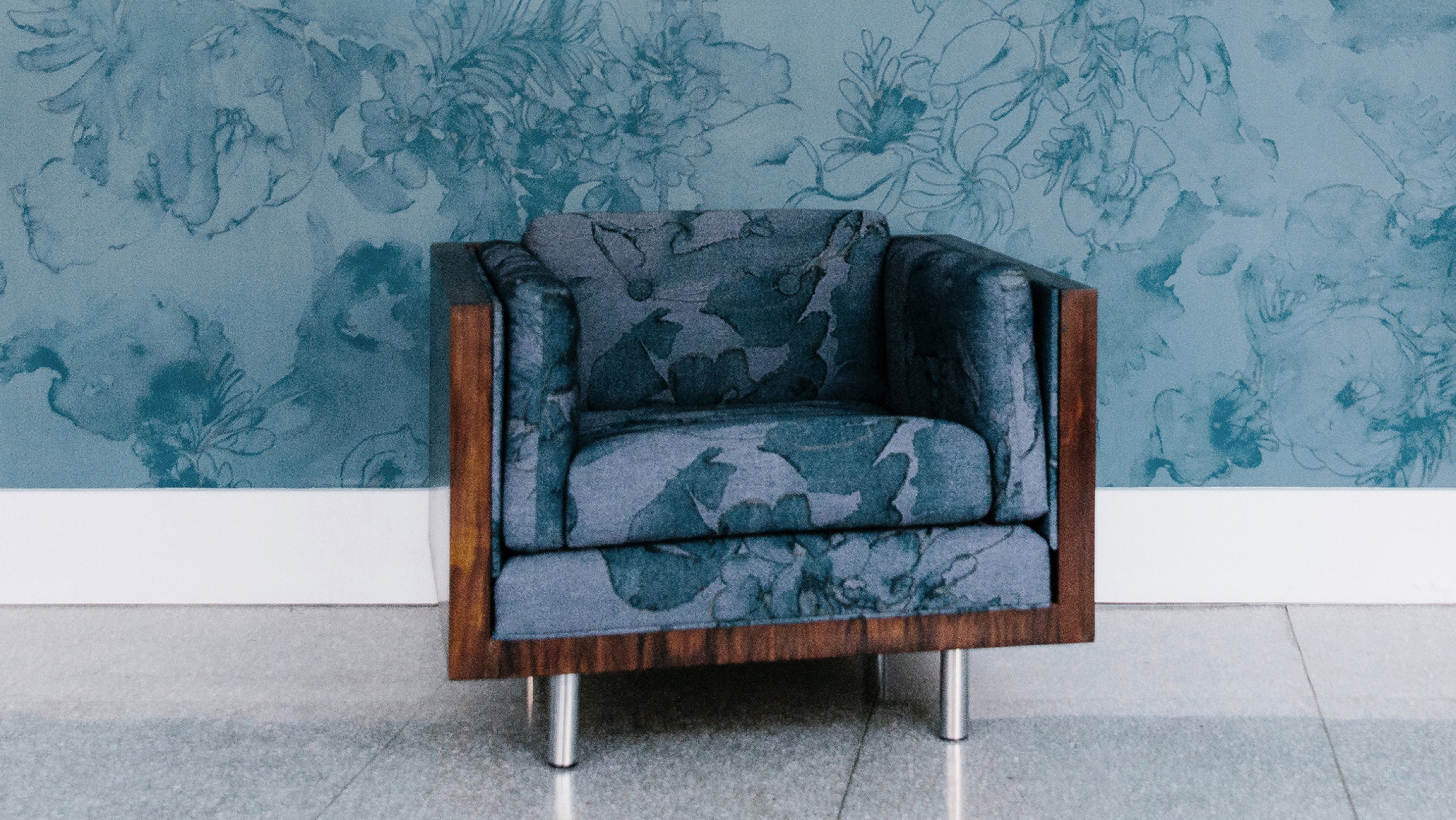 A chair in front of a blue floral wallpaper