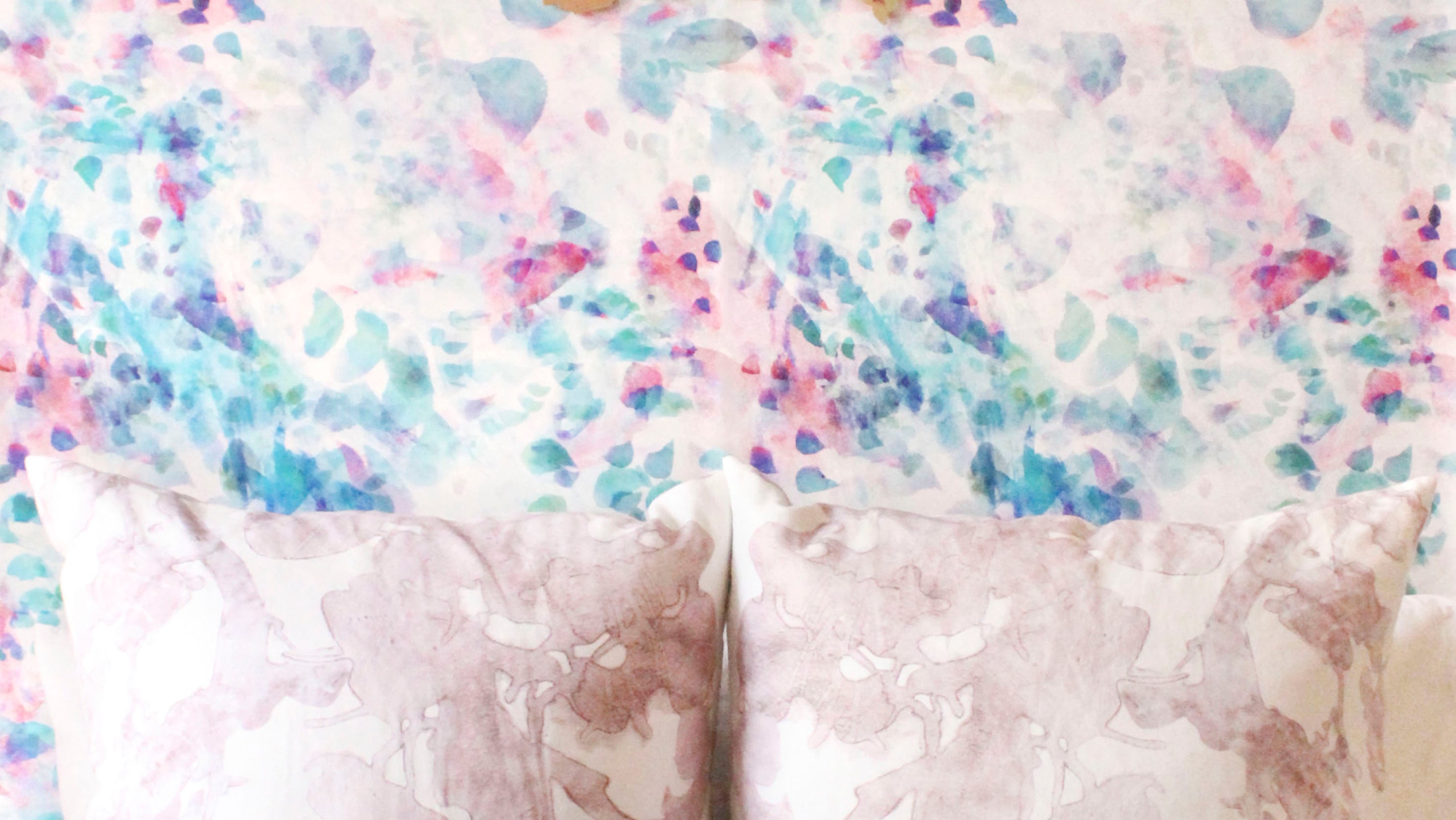 A bed with pillows in front of watercolor wallpaper