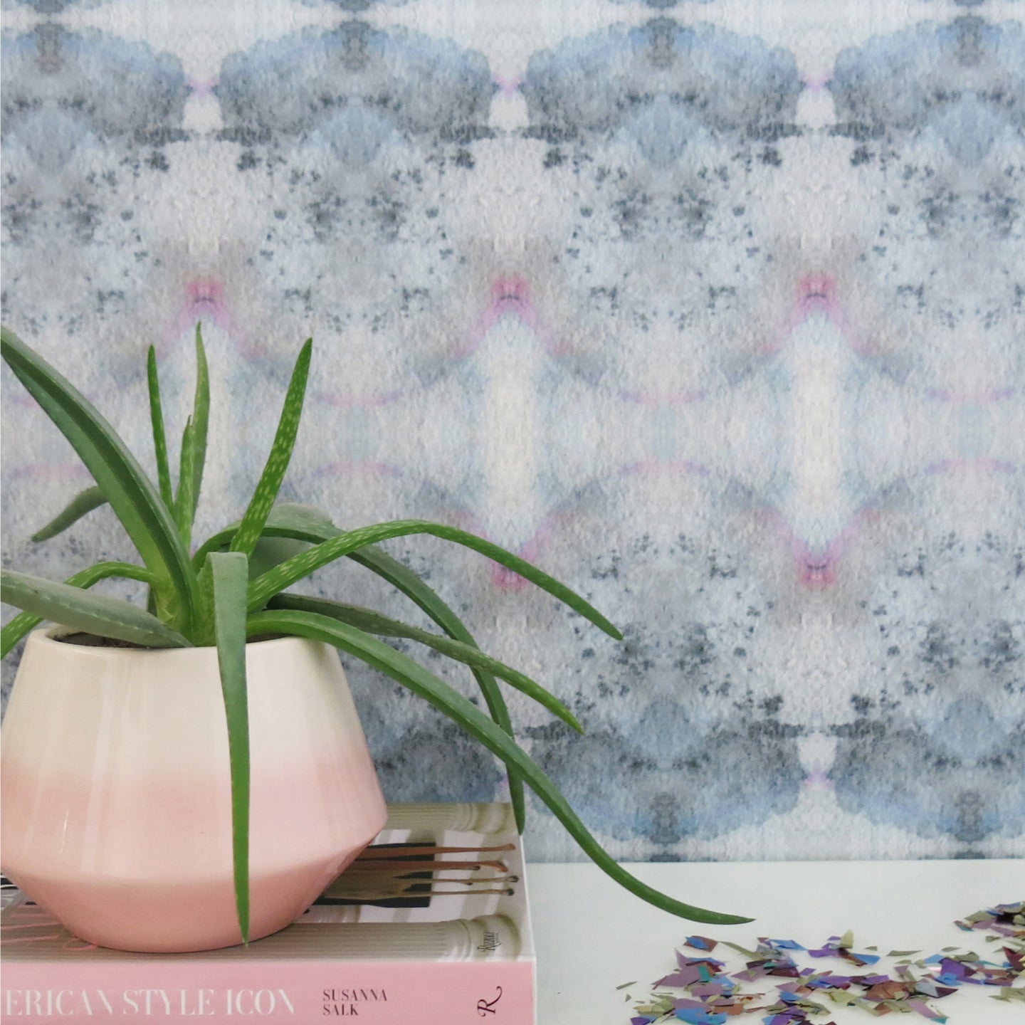 A pink potted plant sits on a table next to a blue wallpaper