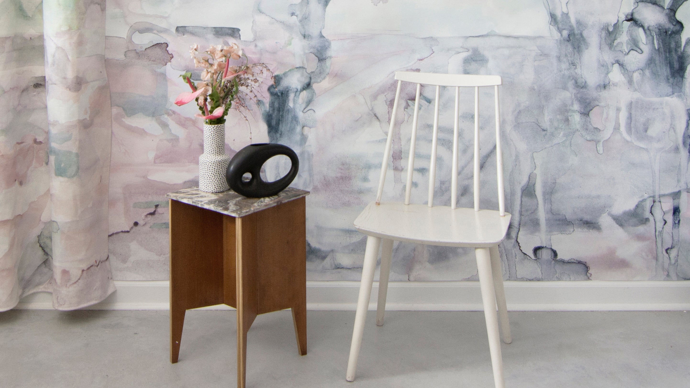 A chair with a vase in front of a watercolor wall