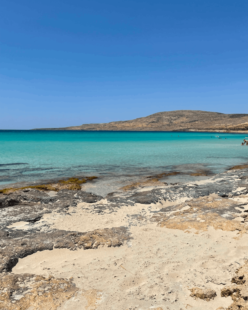 A beach with clear blue water and a rocky shore