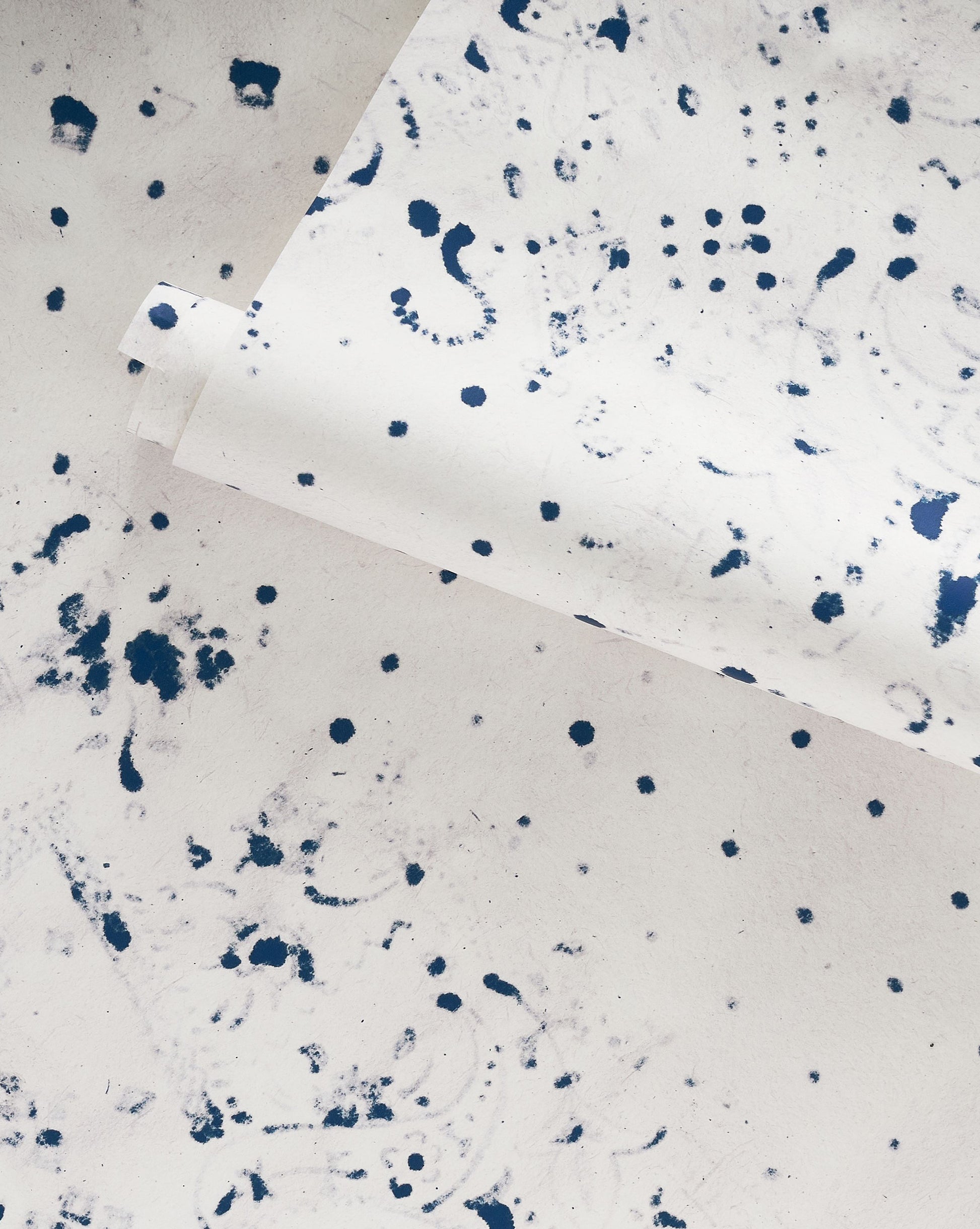 A playful Bandanarama Wallpaper Indigo with polka dots on a white and blue paper with splatters on it