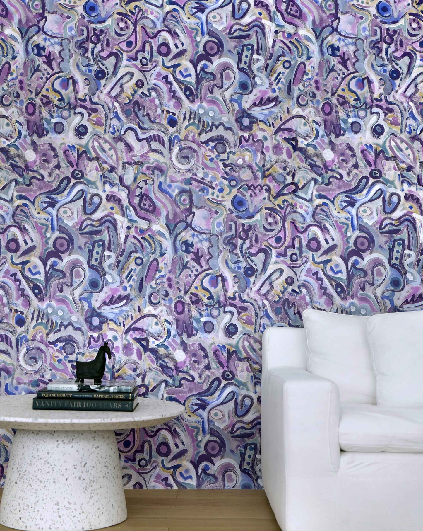 Eskayel's Floripa wallpaper in the colorway Pomegranate in shades of purple installed in a living room with a white couch and a circular side table.