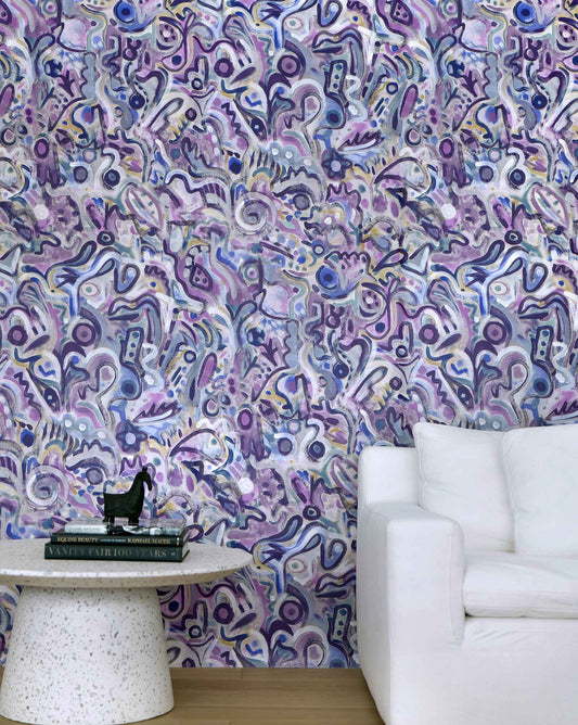 Eskayel's Floripa wallpaper in the colorway Pomegranate in shades of purple installed in a living room with a white couch and a circular side table.