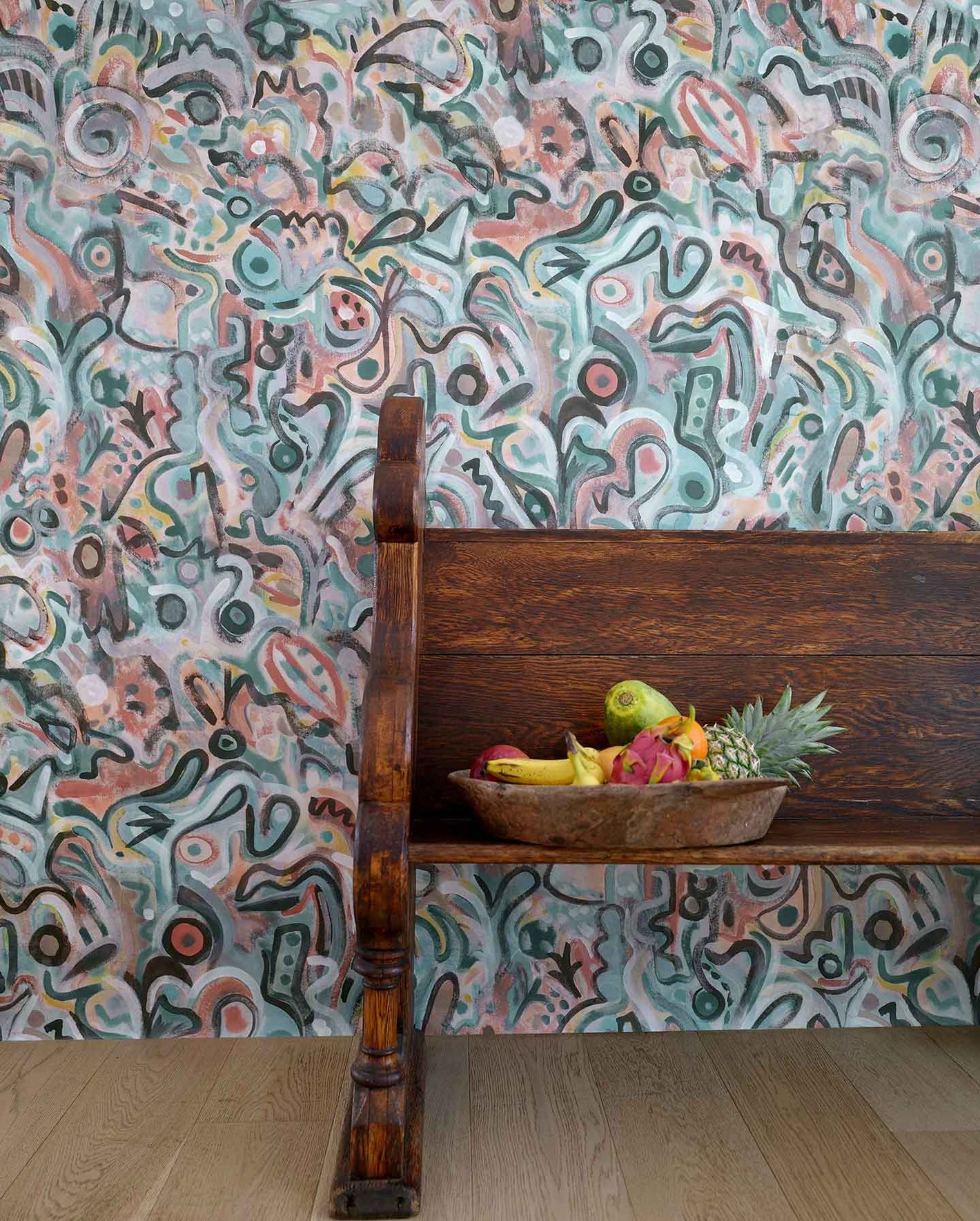 Floripa wallpaper in reef installed in a room with a wood bench and a fruit basket.