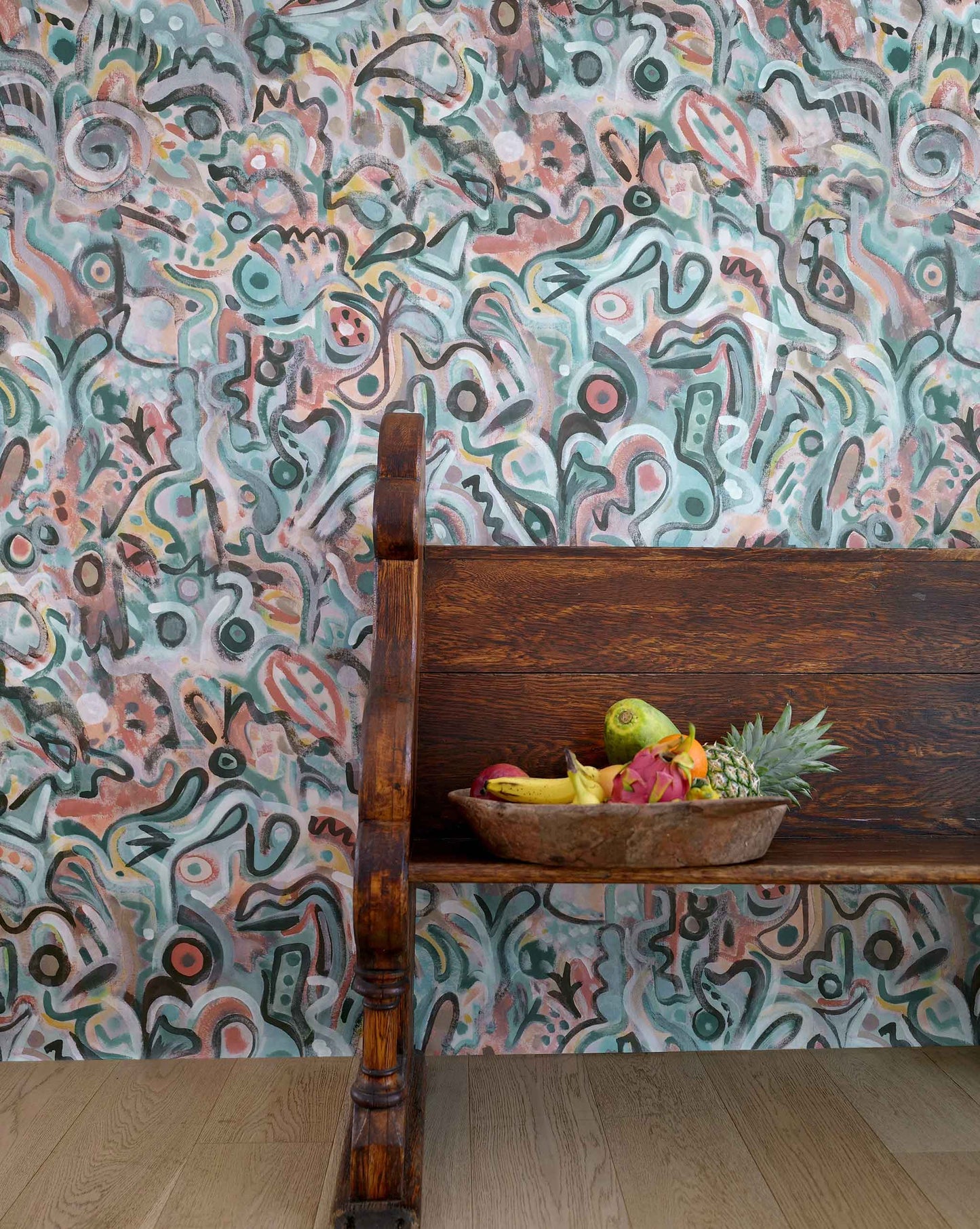 Eskayel's Floripa wallpaper in the colorway Reef in shades of salmon and turquoise installed in a room with a wooden bench.