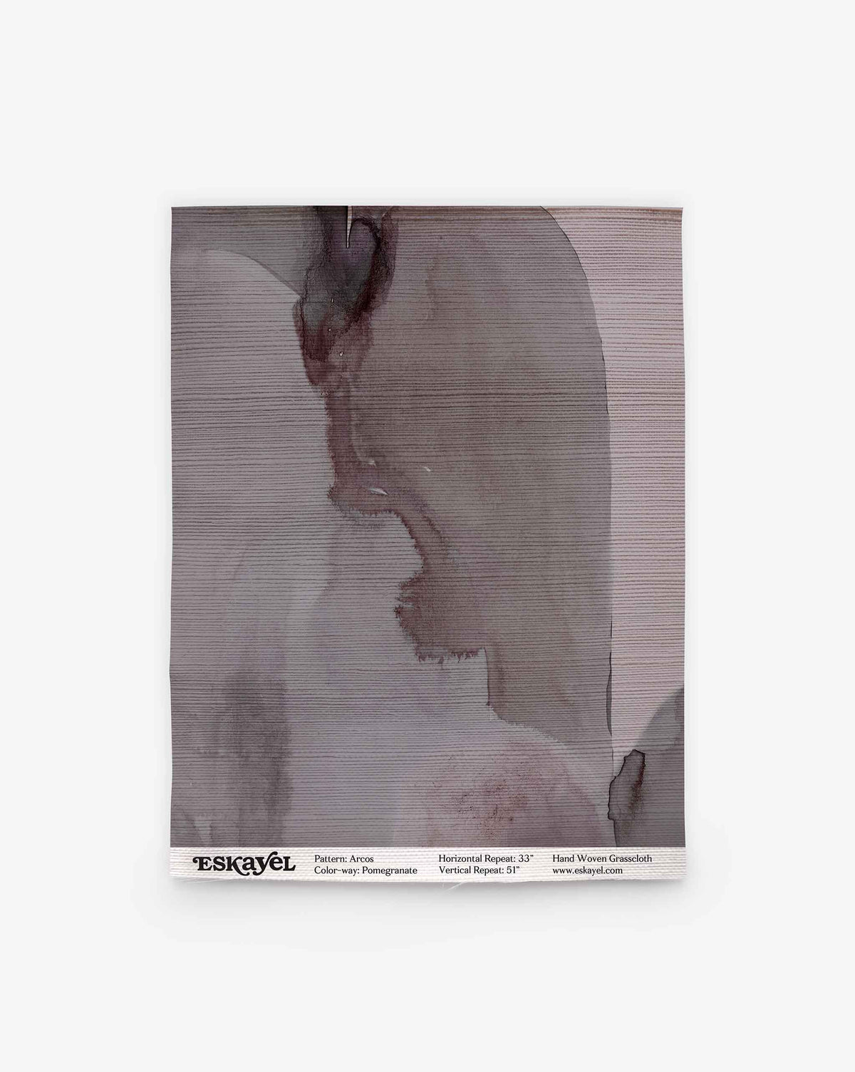 An Arcos Grasscloth Sample in Pomegranate, showing a rectangular piece of textured wallpaper with an abstract grey watercolor design and a product label along the bottom edge.