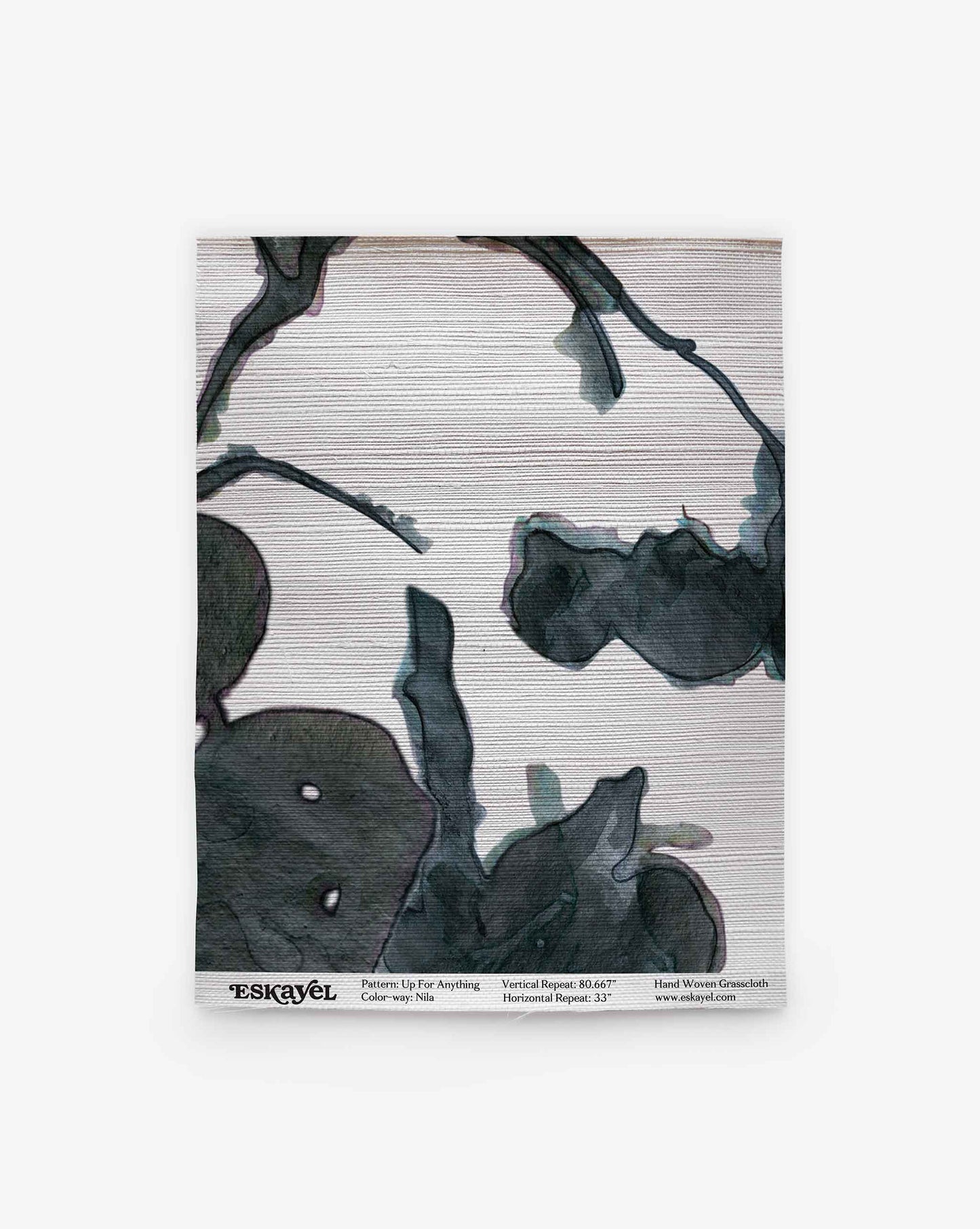 A textile sample labeled “Up for Anything Grasscloth||Nila” features a dark green abstract botanical pattern on a light background, with product information along the bottom edge, evoking the sophisticated look of a monochrome wallcovering.