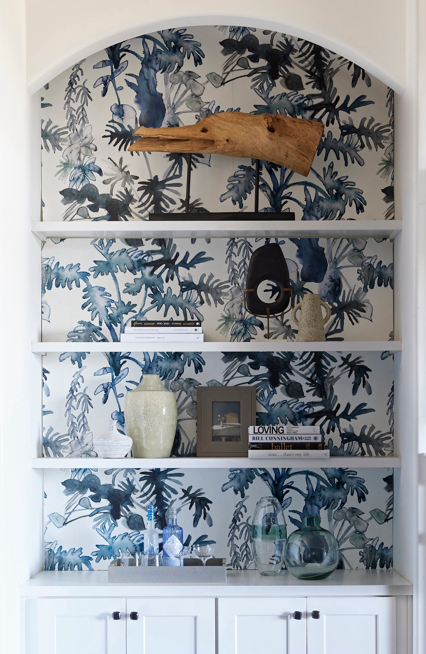 Our Topiary Wallpaper in Indigo with a botanical pattern in blue hues is installed as the backdrop of a shelf.