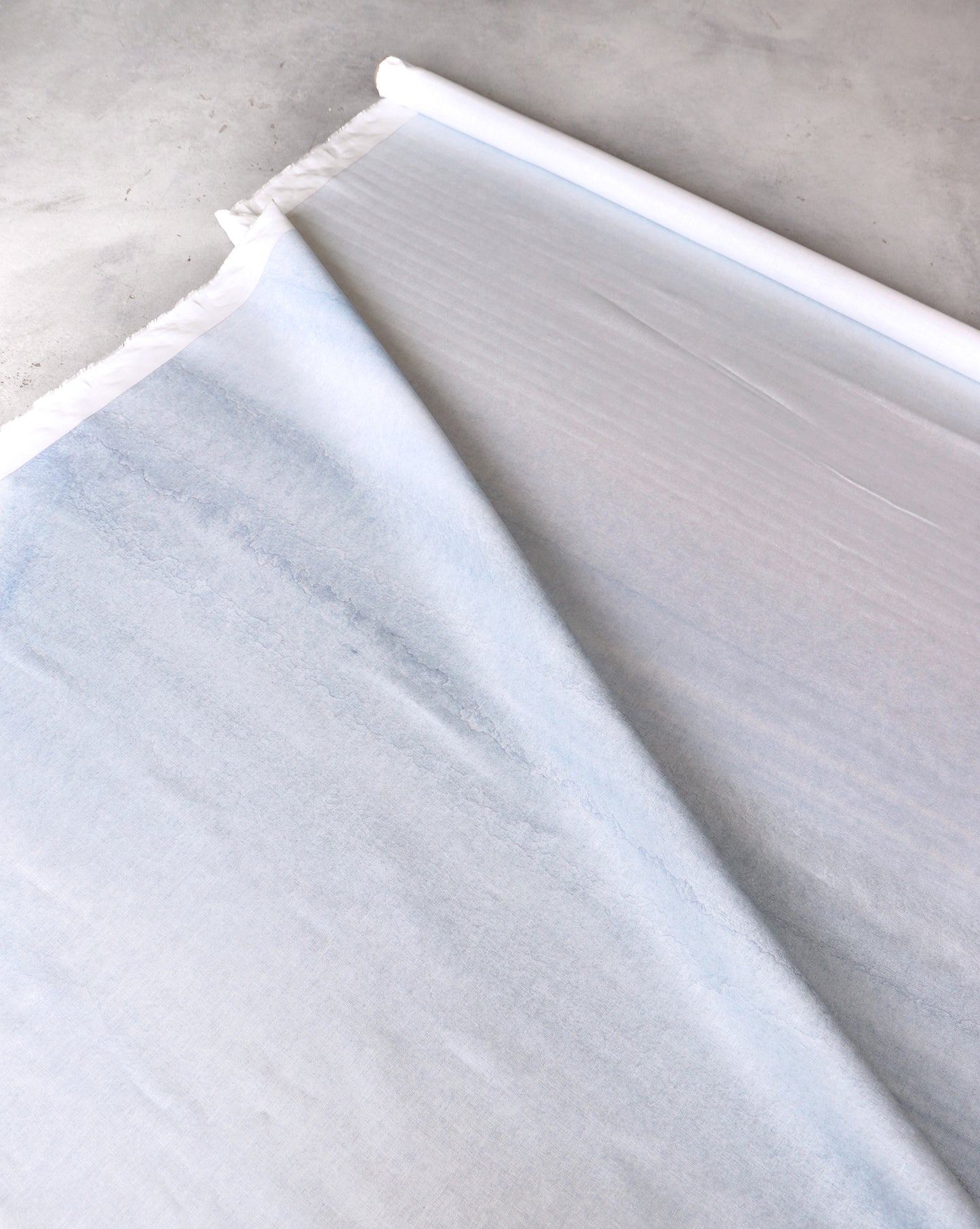 A partially unrolled roll of Lily's View Fabric in the Dawn color, 54" wide, rests on a gray surface.
