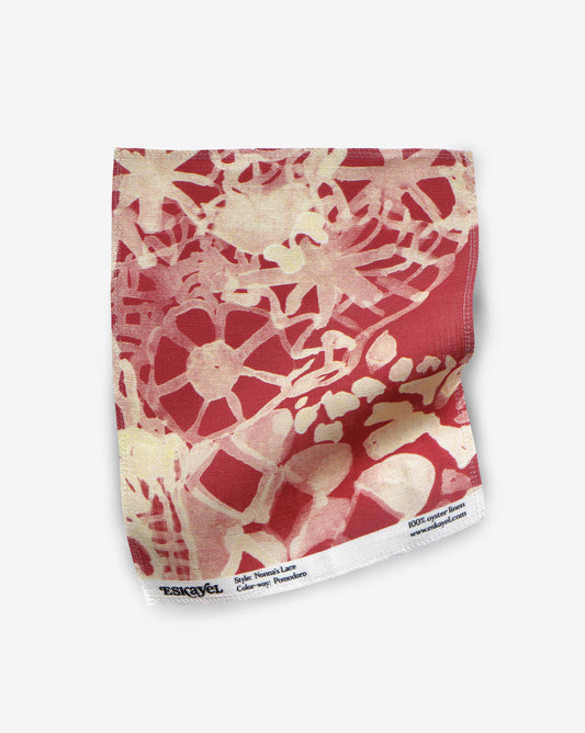 A fabric swatch of Nonna’s Lace in warm Pomodoro shows a closeup of the design in a palette of reds.