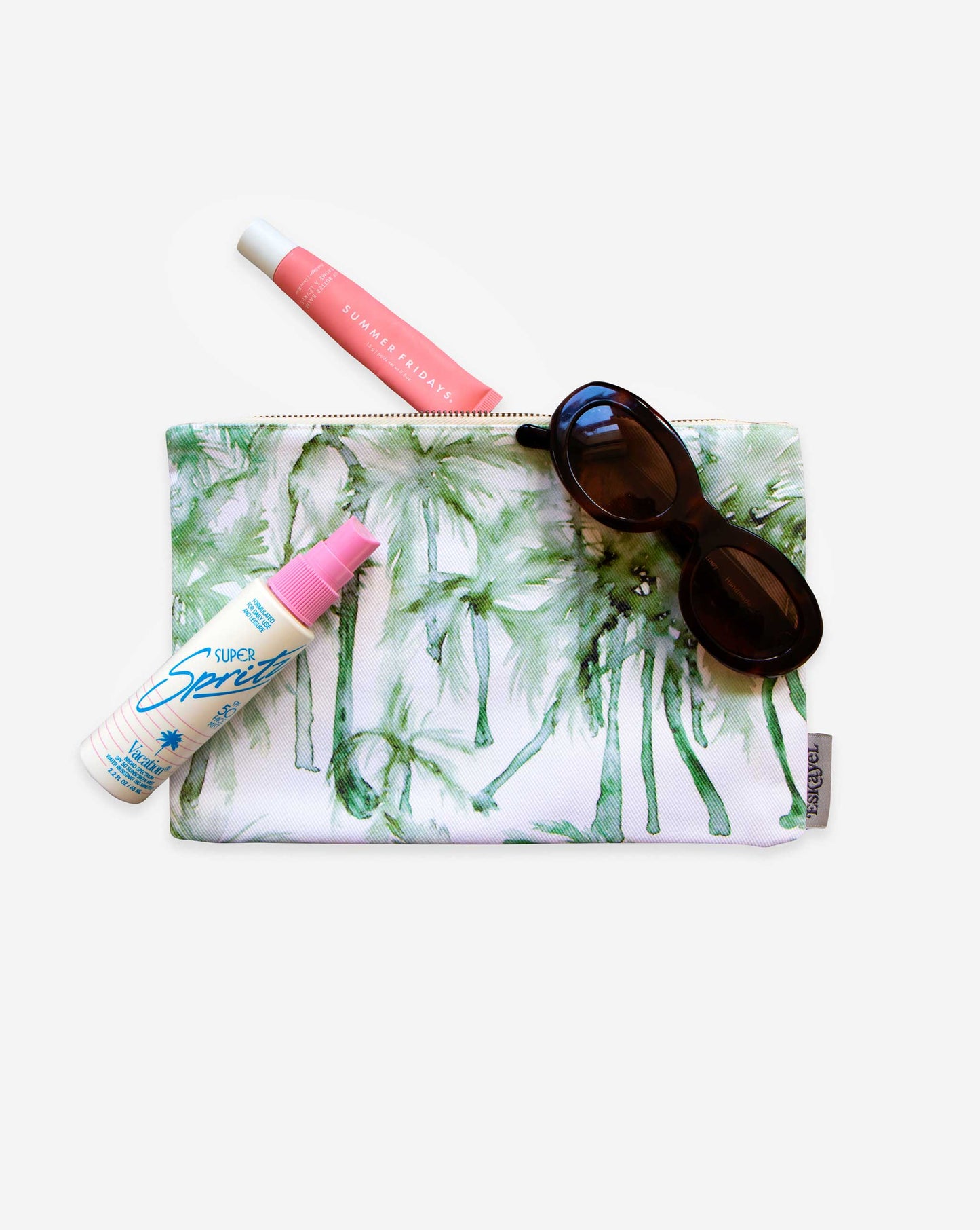 The Chloros Palm Dance Pouch brings a tropical vibe, with chic sunglasses, pink lip products, and sunscreen spray neatly arranged on a white background. It's perfect for storing all your vacation essentials in style.