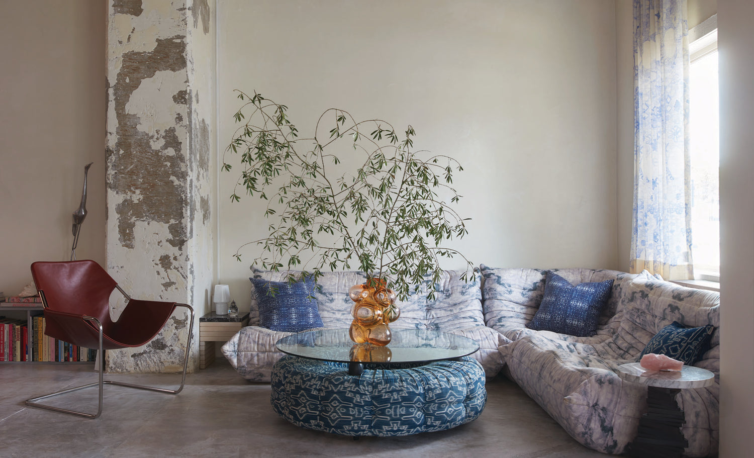 A sitting area with a fabric based coffee table, patterned sofa, and a plant.