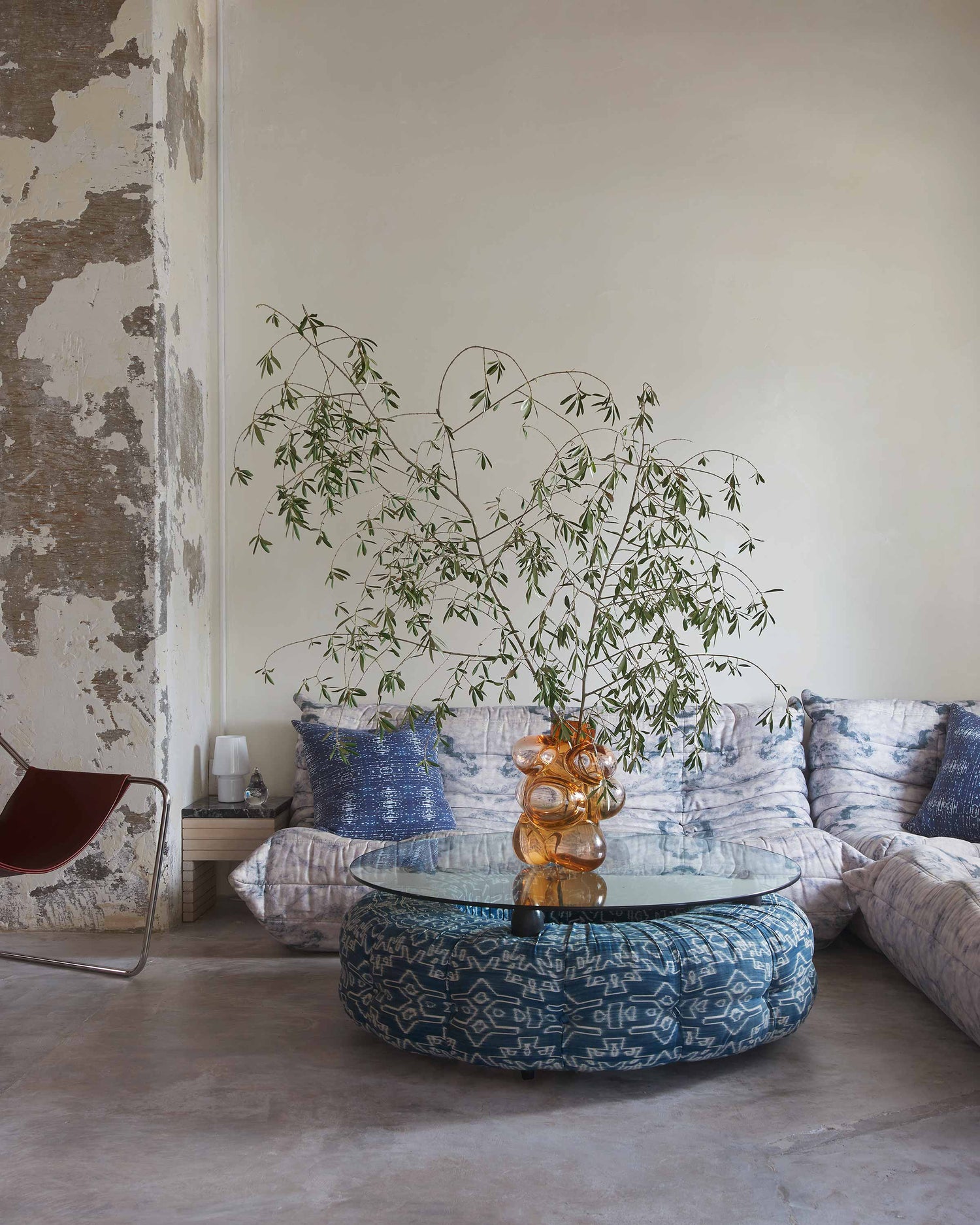Living room with a glass coffee table, patterned ottoman, and decorative pillows.