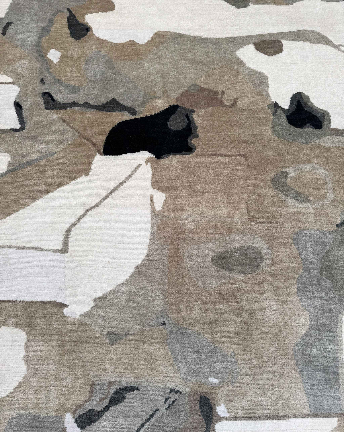 Abstract area rug with an organic, painterly pattern in beige, taupe, gray, off-white, and black.