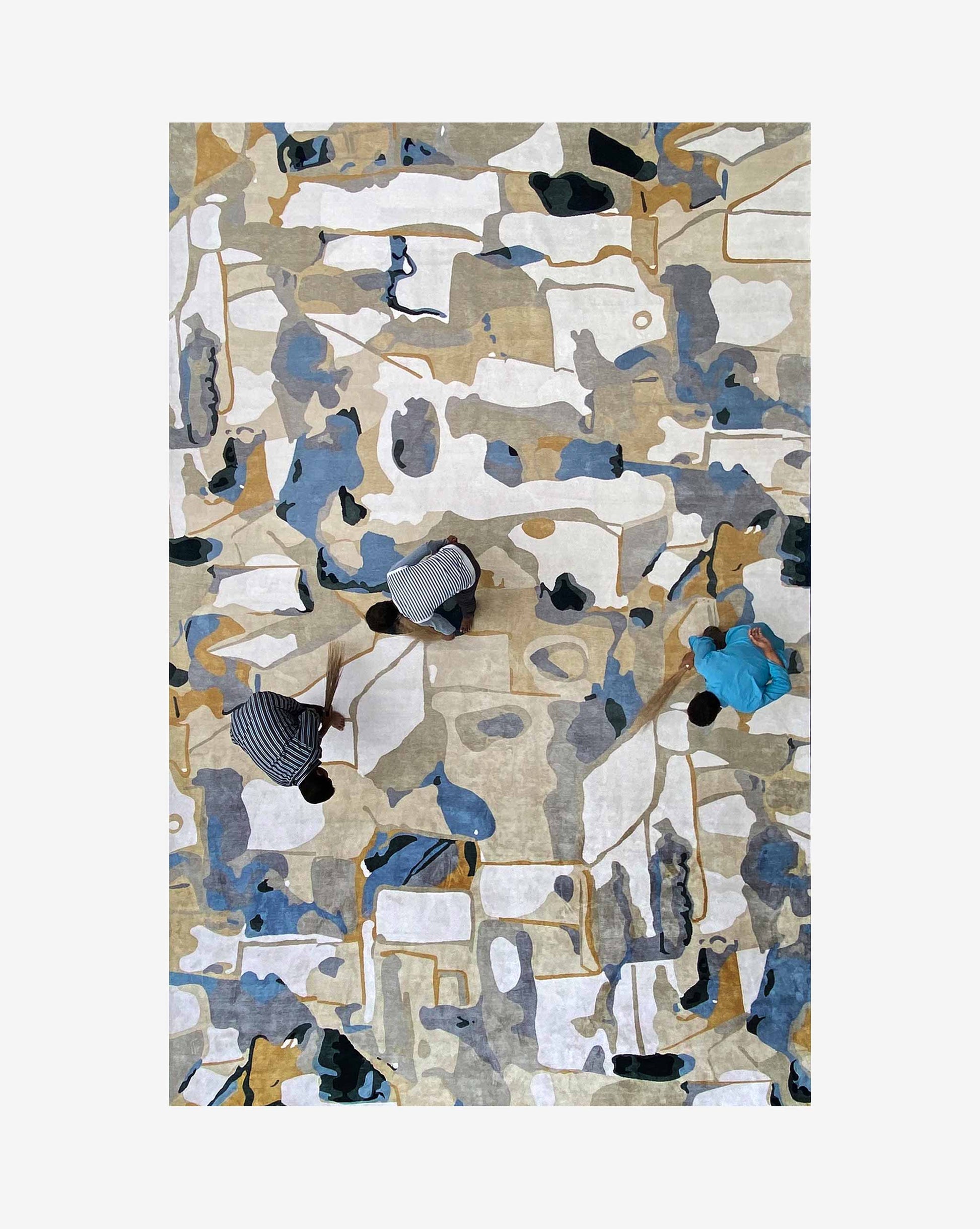 Three people, seen from above, walk across the Medina Hand Knotted Rug||Blanca CUSTOM. Two wear striped clothing and one is dressed in blue, highlighting the rug’s intricate Marrakesh-inspired pattern.