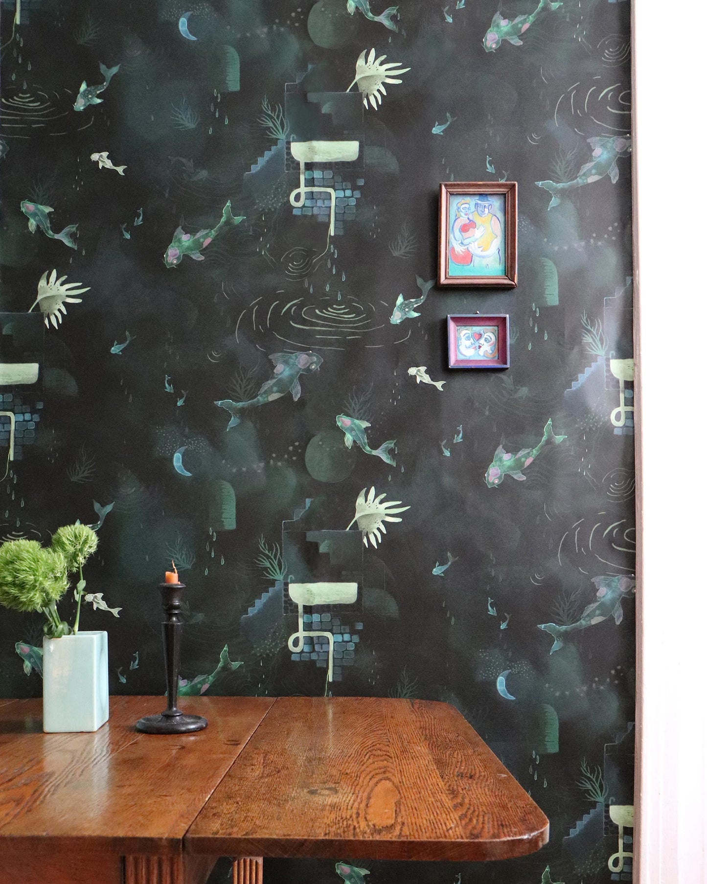 A table with a candle and a picture on the wall, adorned with Water Signs Wallpaper||Emerald.