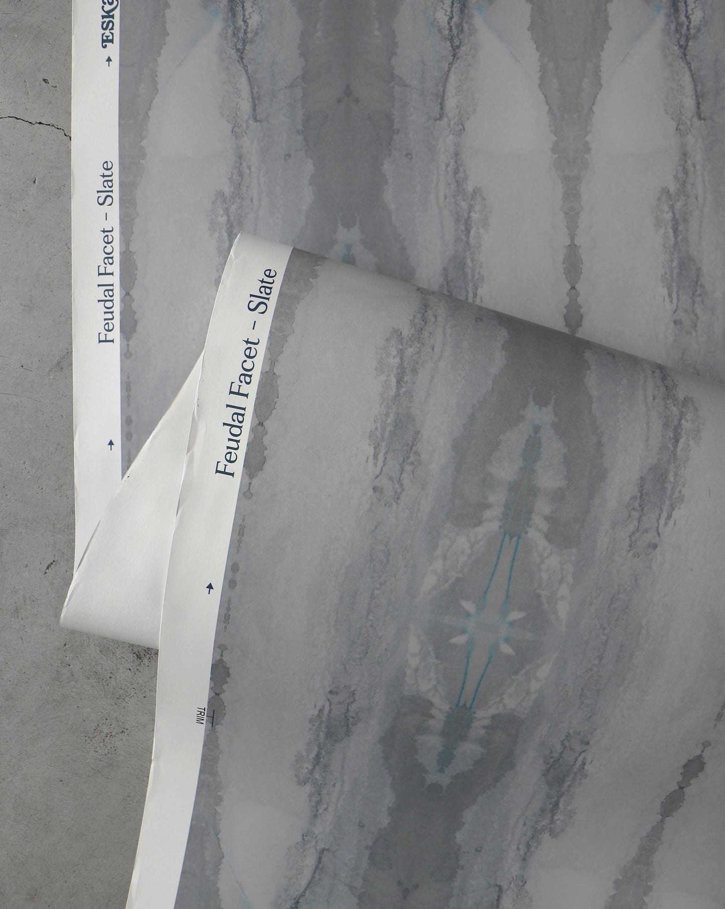 Two rolls of grey and white patterned wallpaper with a text label reading "Feudal Facet Wallpaper||Slate" partially visible along the edges, showcasing an exquisite fabric and wallpaper design reminiscent of Tuscany.
