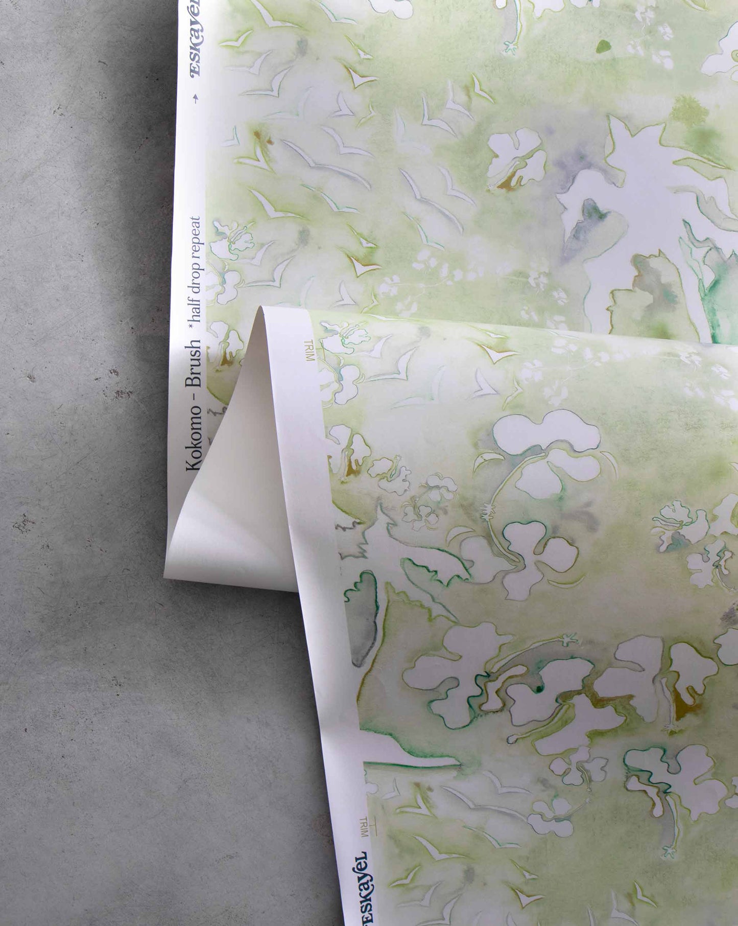 An image of Kokomo Brush Wallpaper with green tones. The pattern is inspired by a tropical landscape of hibiscus lilies, birds, and palm trees using this idea to create one continuing line.