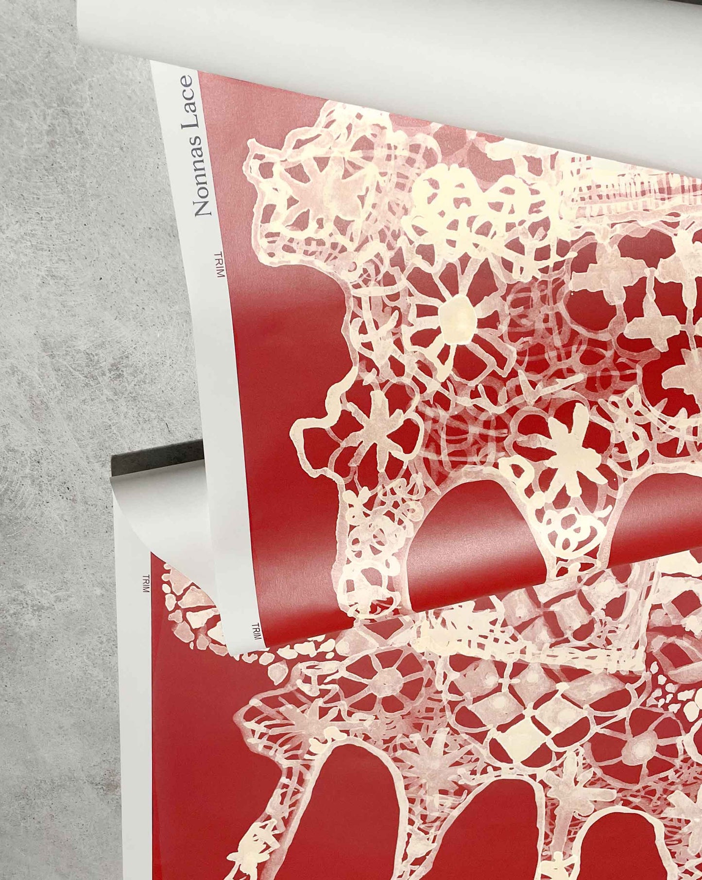 An open magazine displays the Nonna's Lace Wallpaper in Pomodoro, featuring delicate white lace-like patterns. The magazine lies elegantly on a gray surface.