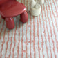 A red chair on a Drippy Stripe Hand Knotted Rug 6' x 9' Sienna next to a cactus