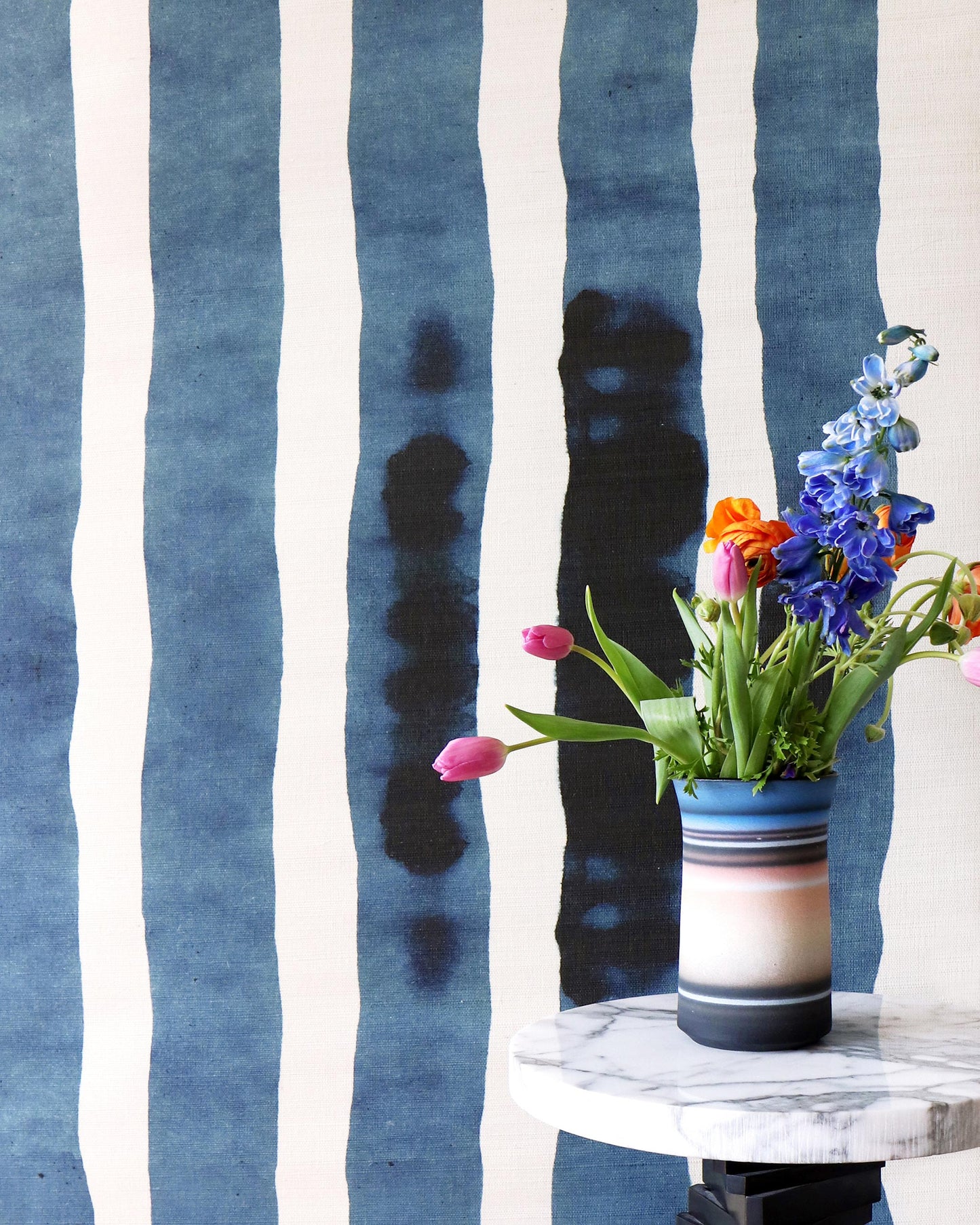 A vase of flowers on a marble table in front of a Bold Stripe Grasscloth Azure wall