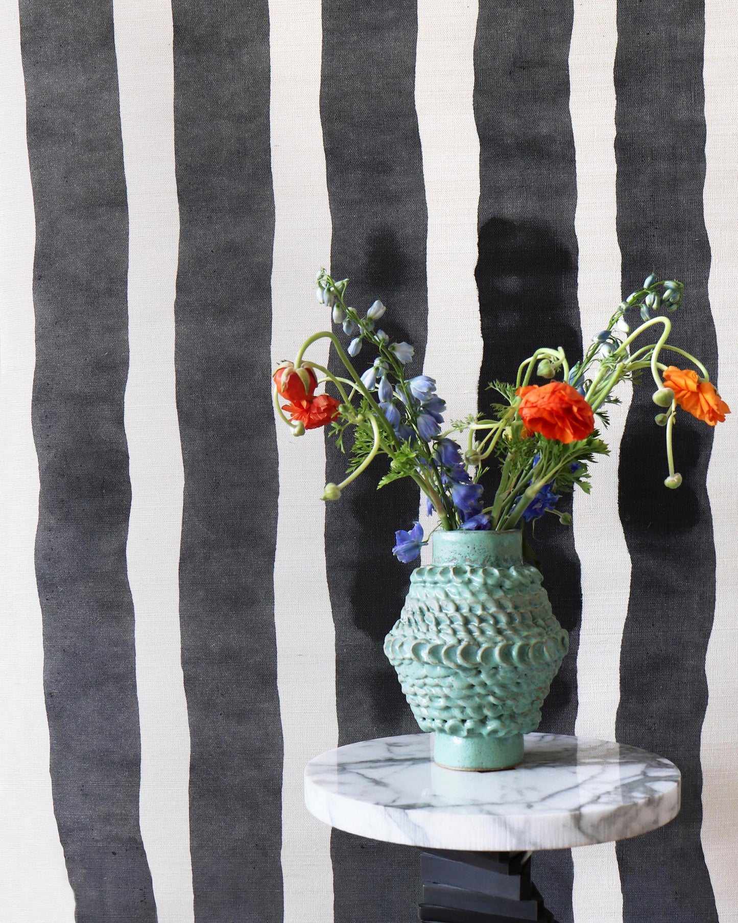 A vase of flowers on a table in front of a black and white striped Bold Stripe Grasscloth Slate wall