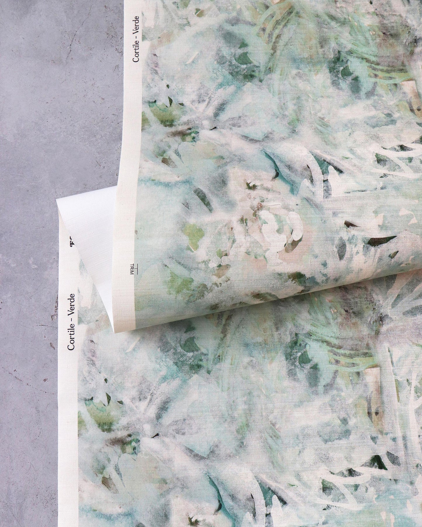 A piece of Cortile Grasscloth Verde with a watercolor pattern of green and white flowers on it