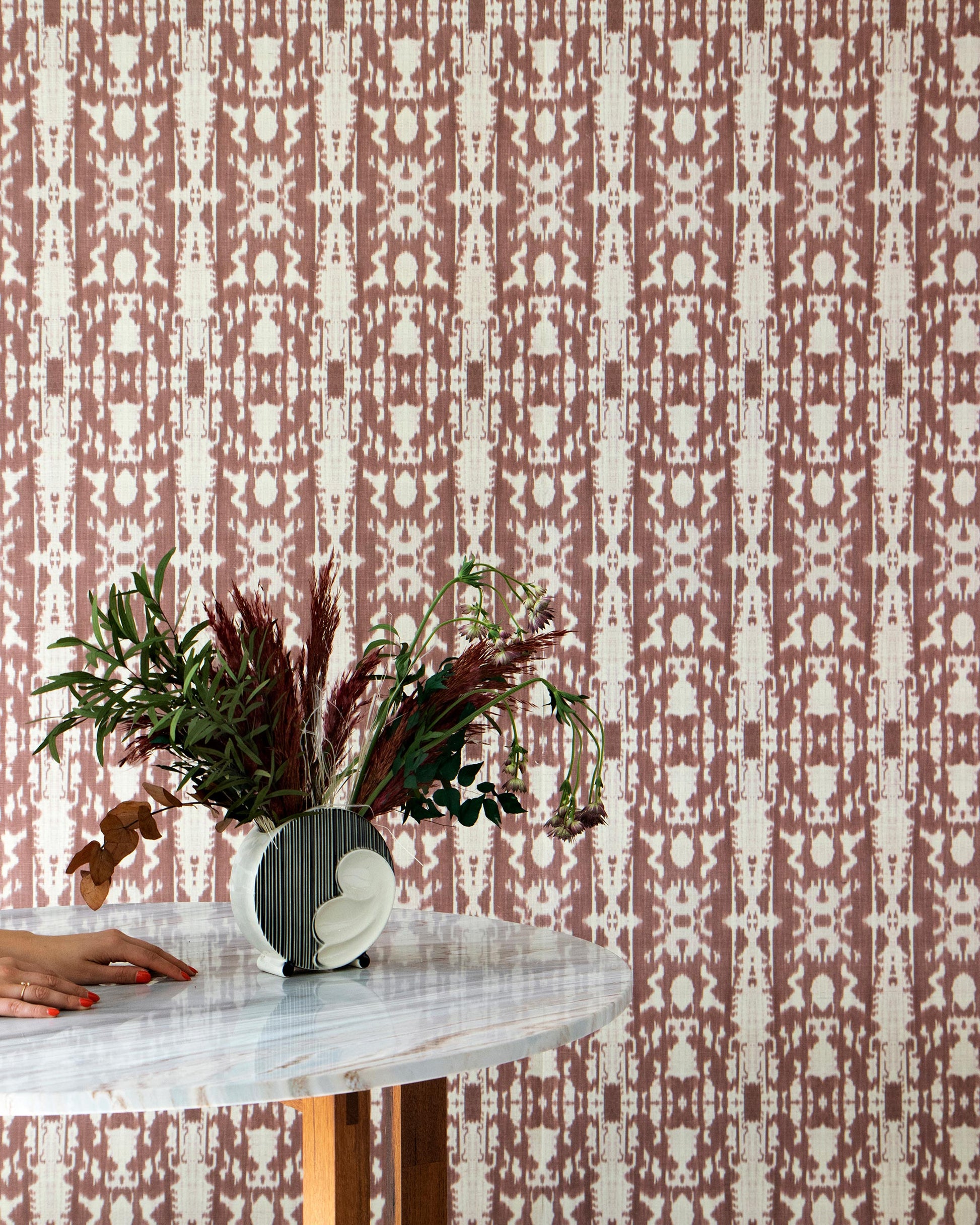 A woman is sitting at a table with a vase of flowers, surrounded by Biami Grasscloth