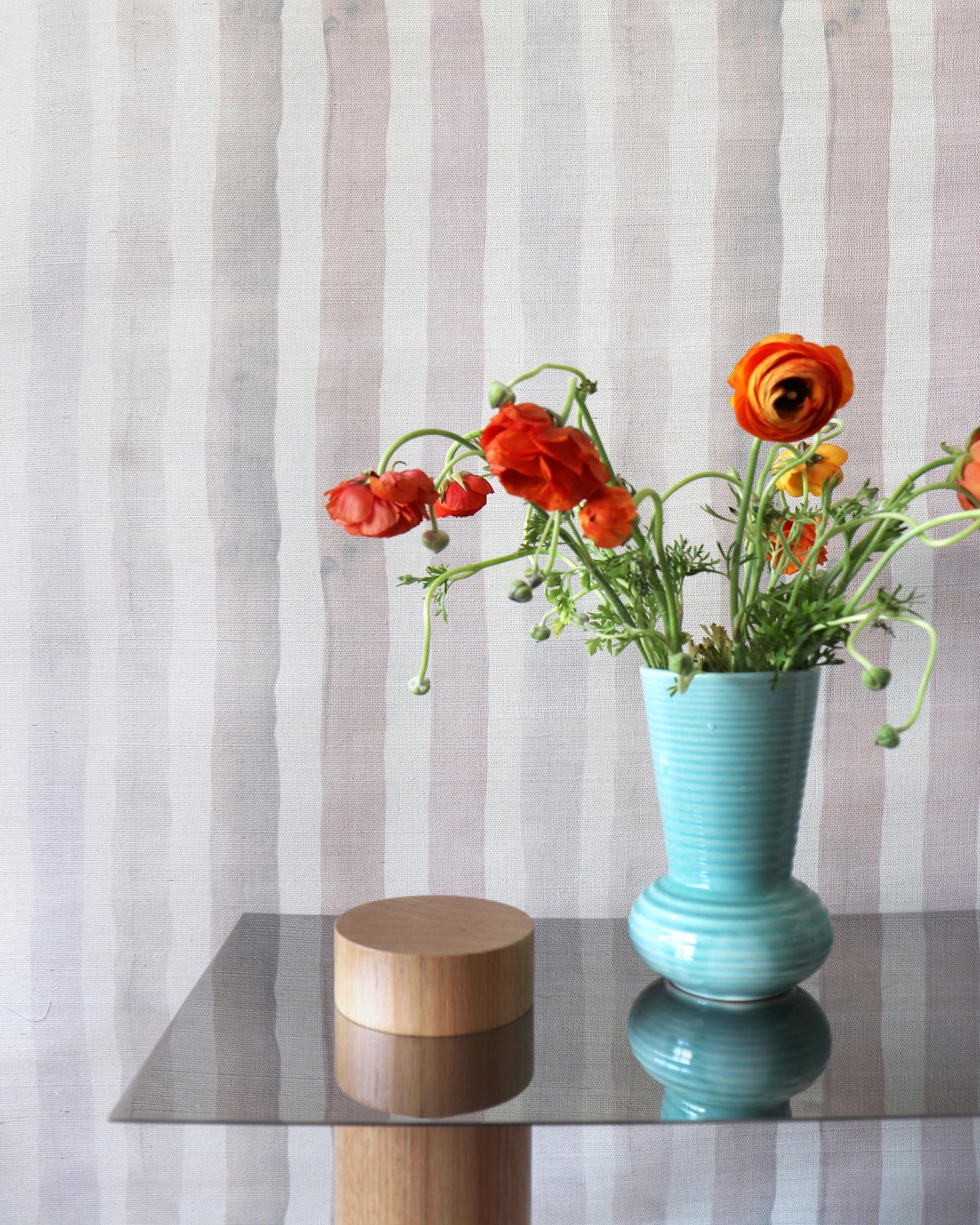 A vase of orange flowers on a table with a Gradient Stripe Grasscloth Pink Island behind it