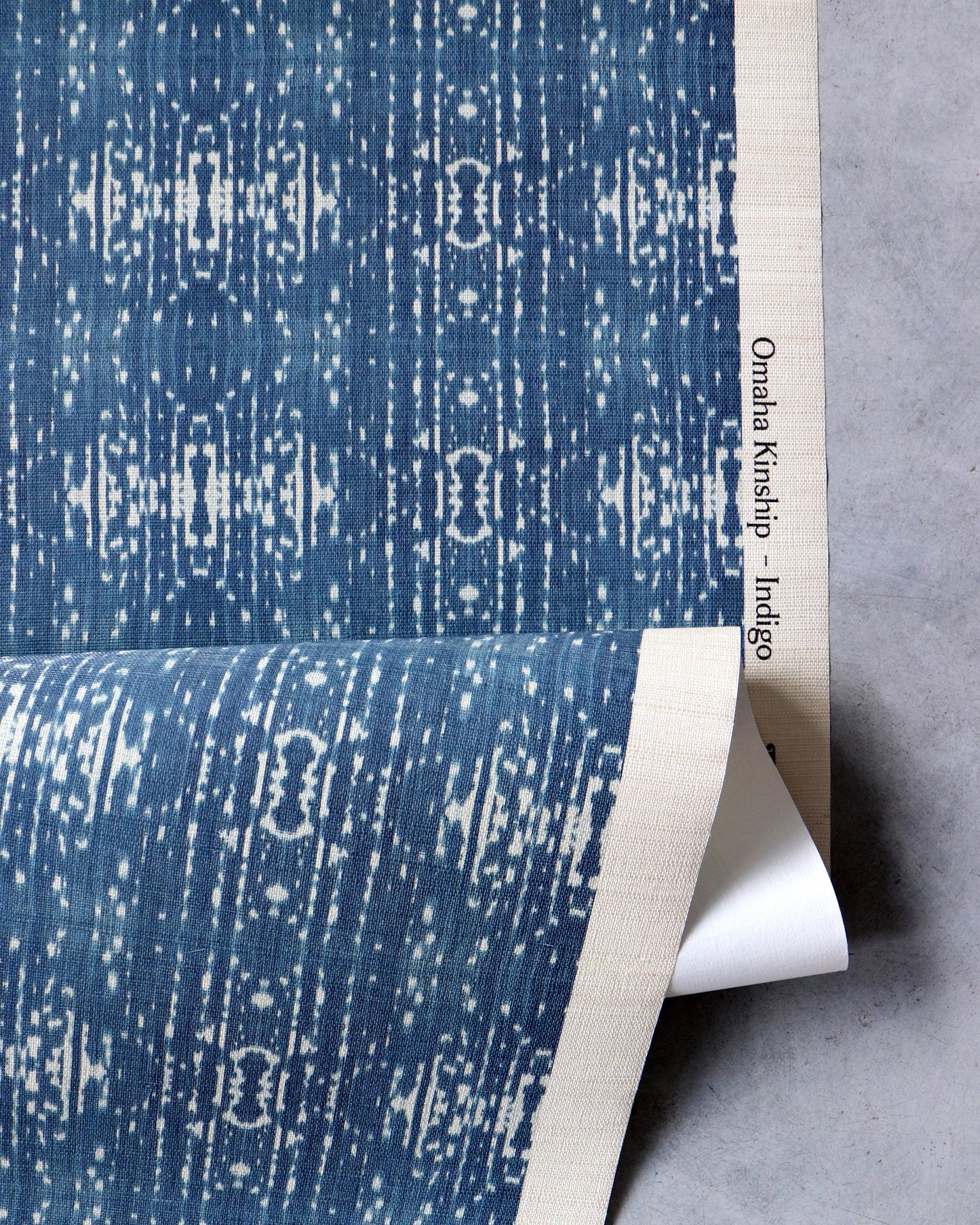 A blue and white fabric in an Omaha Kinship Grasscloth Indigo ikat colorway with Eskayel's Kinship pattern