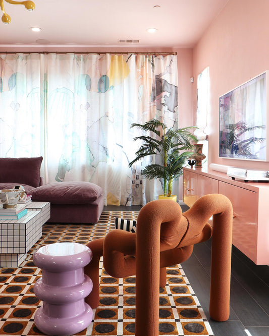 A living room with Sea Galaxy Fabric Reef drapes and a mural artwork on the pink walls