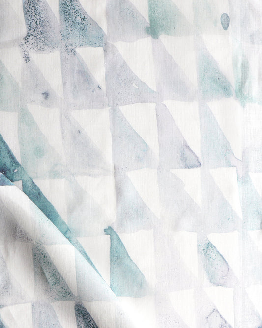 A close up of Triangle Checks Fabric Verde, a white fabric with a geometric pattern