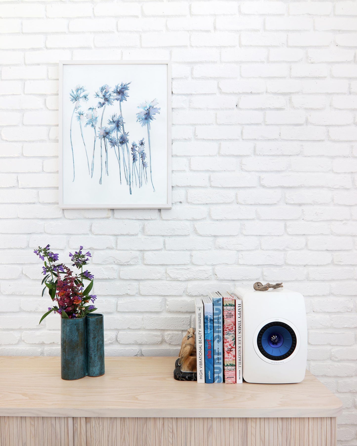 A white bookcase with So Cal Print artworks and a vase of flowers
