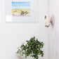 A Shore Pine Print of a desert scene, created by the artist, hangs above a wooden stool