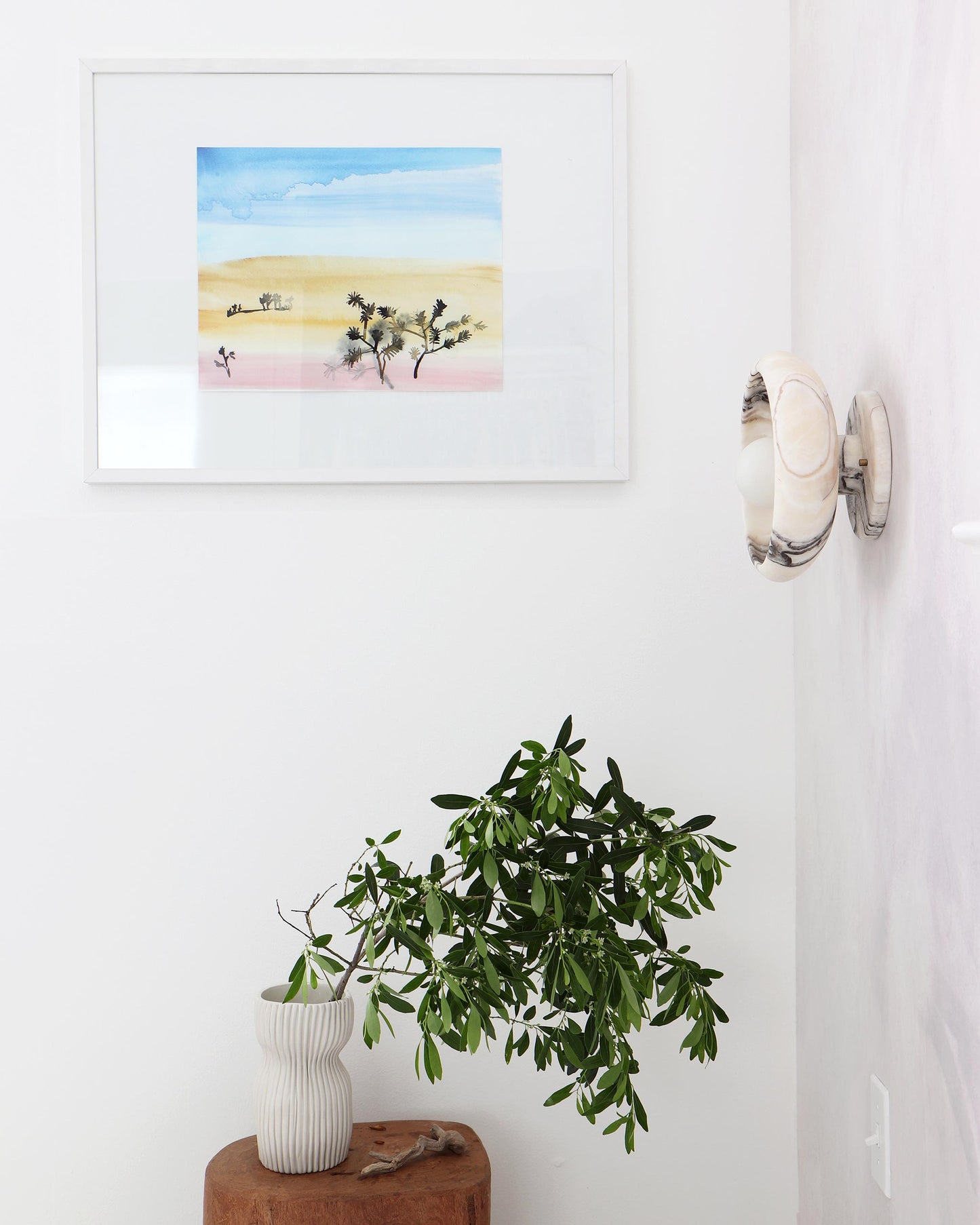 A Shore Pine Print of a desert scene, created by the artist, hangs above a wooden stool