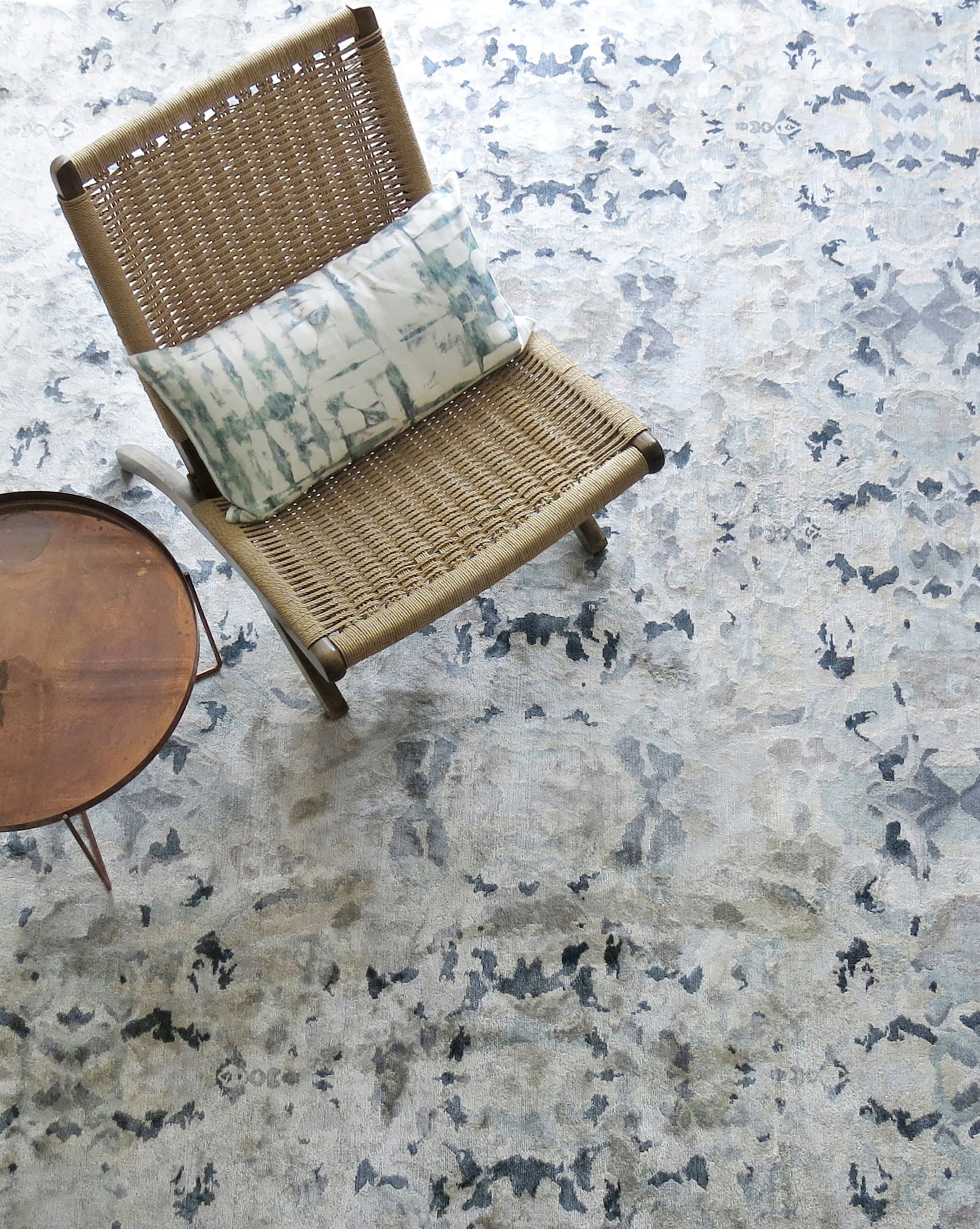 A wicker chair sits on an Alabaster Hand Knotted Rug Light, exhibiting blue undertones