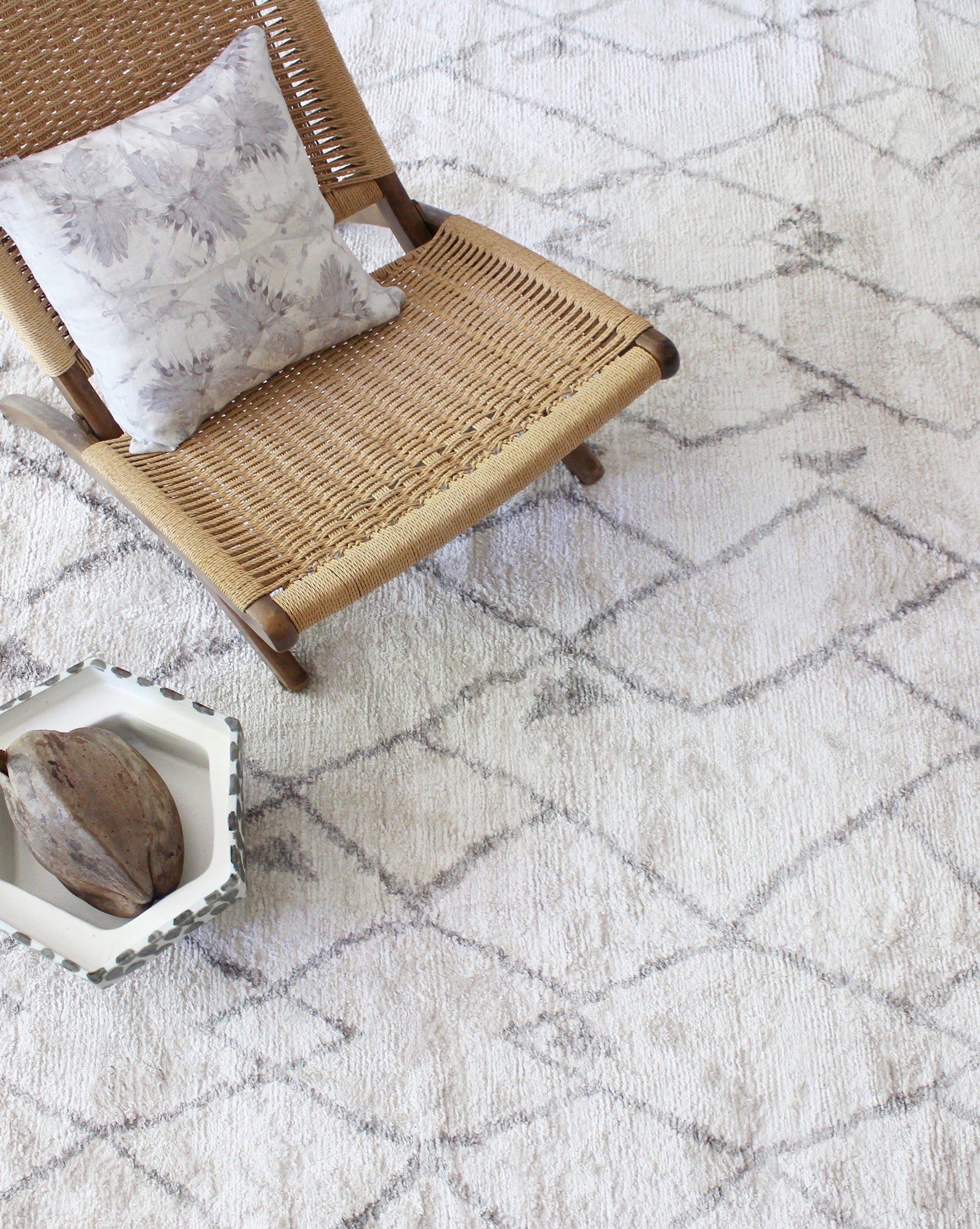 A grey Peaks Hand Knotted rug with a wicker chair on it