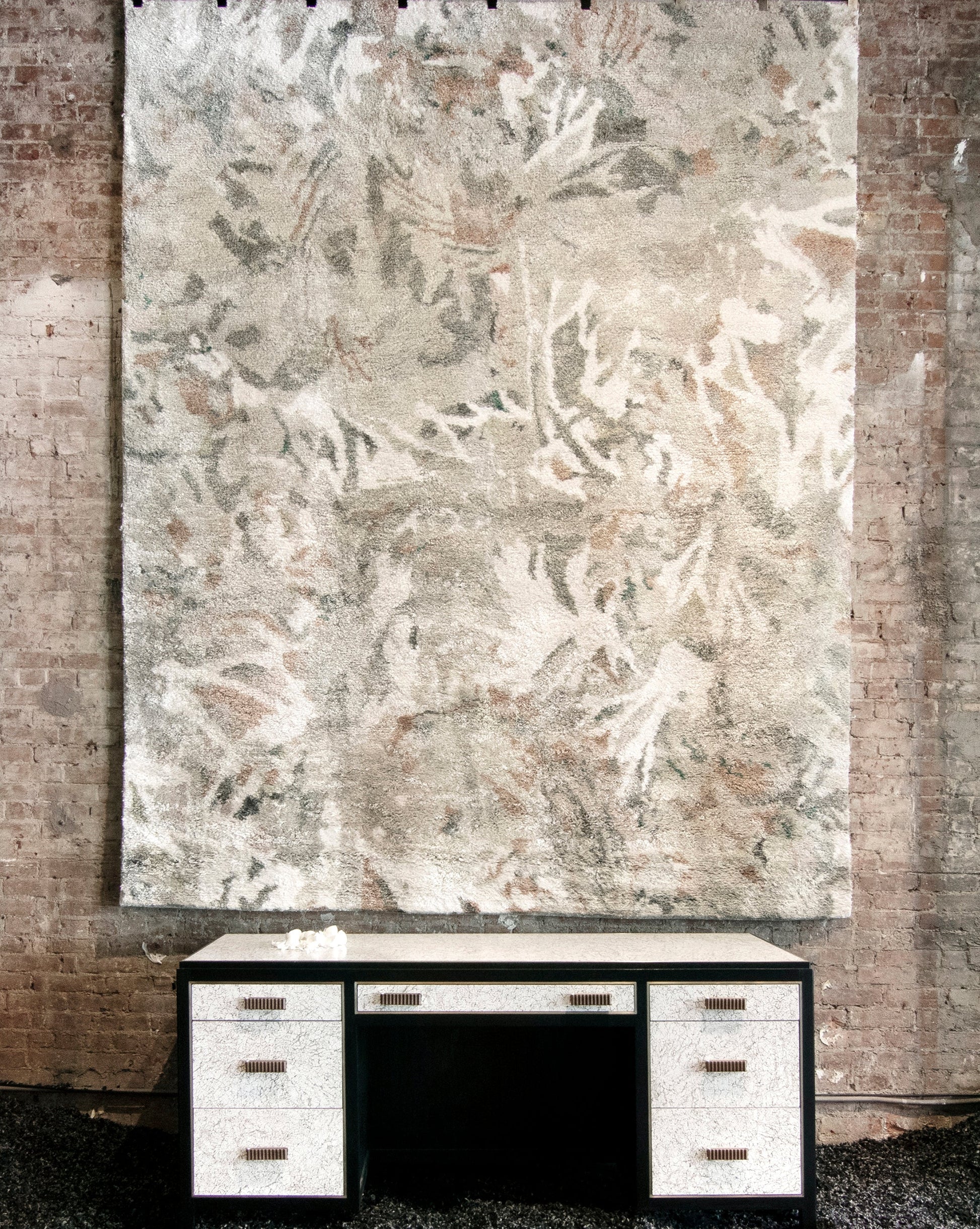 A desk in a room with a large painting on the wall is complemented by the Cortile Hand Knotted Rug Alba, adding texture and pattern to the space