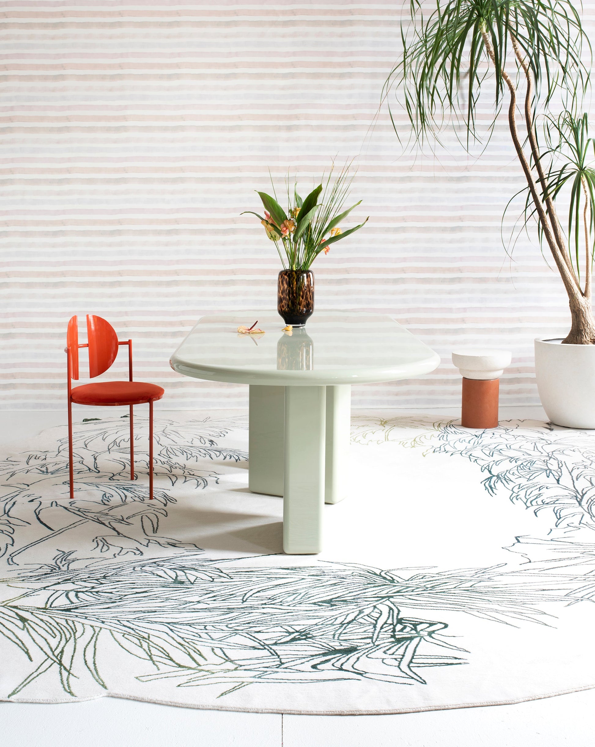 A modern botanical table with a Through The Grove Hand Knotted Rug Neutral design beneath, featuring a white table and a plant on it