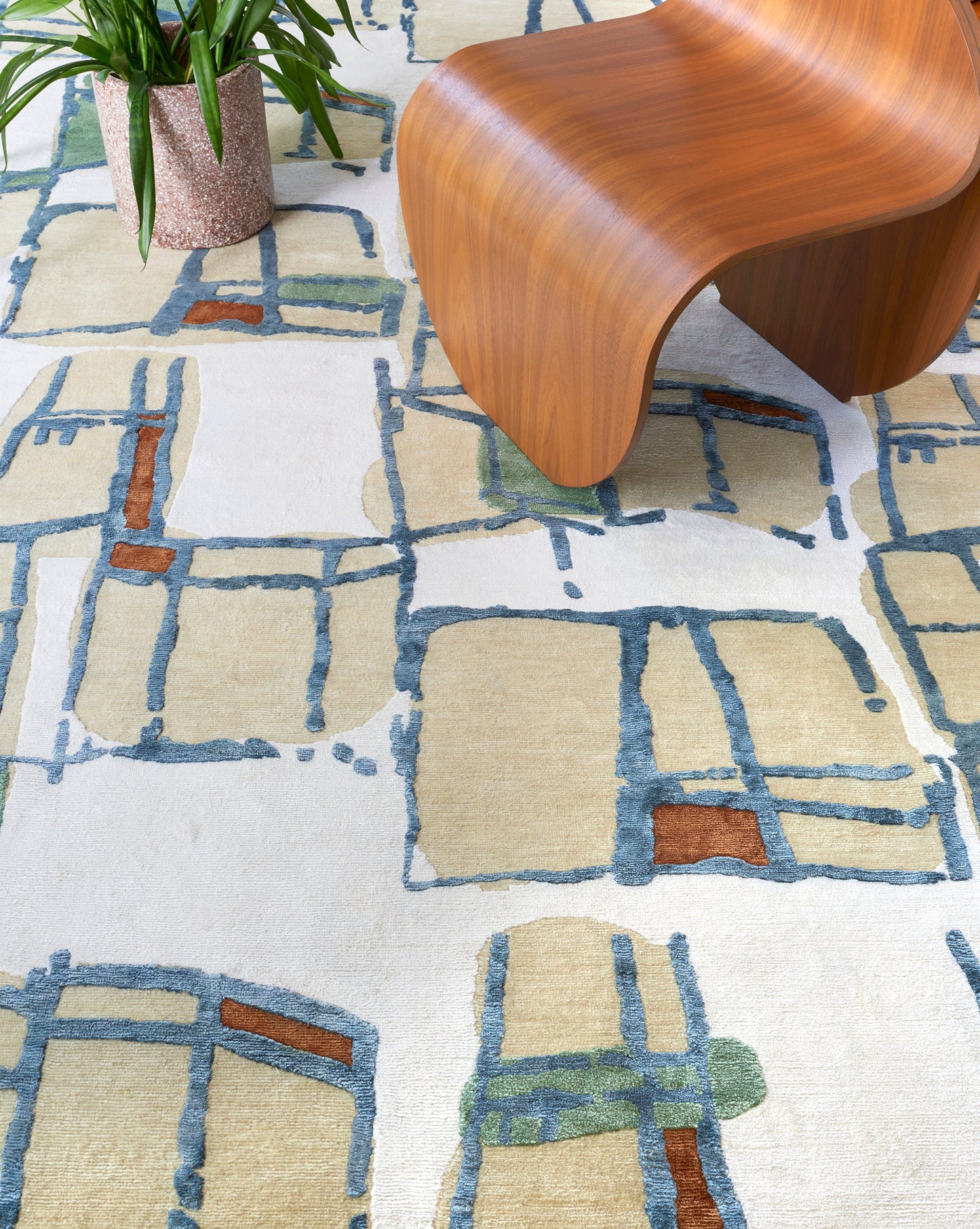 A Quotidiana Hand Knotted Rug Isthmus with an abstract pattern enhances the design process by complementing the wooden chair and a potted plant