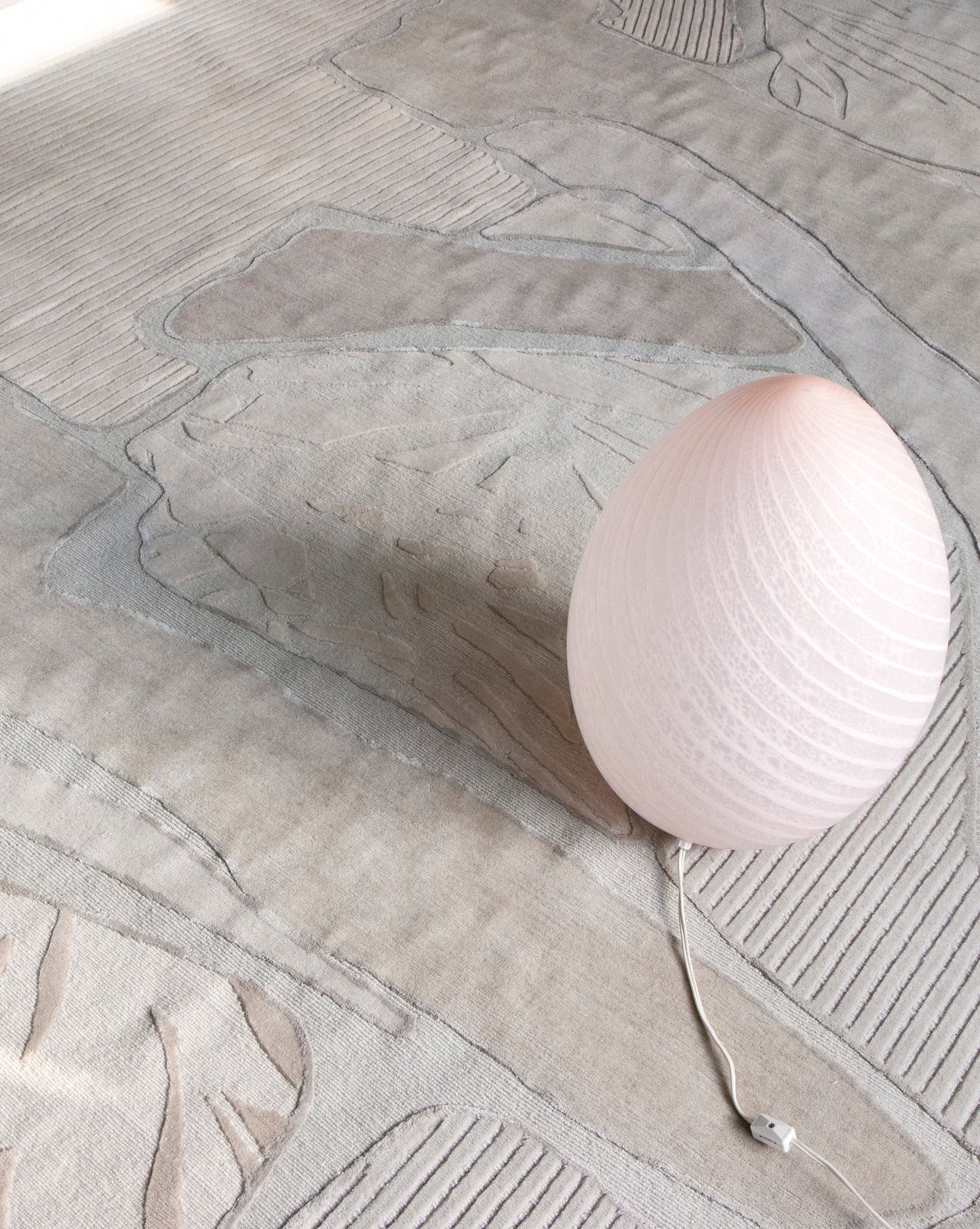 A pink ball sits on top of a Sky Arc Hand Knotted Rug Neutral in the Eskayel studio