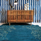 A Through The Grove Hand Knotted Rug Azure from the Salentu Collection in front of a blue wall